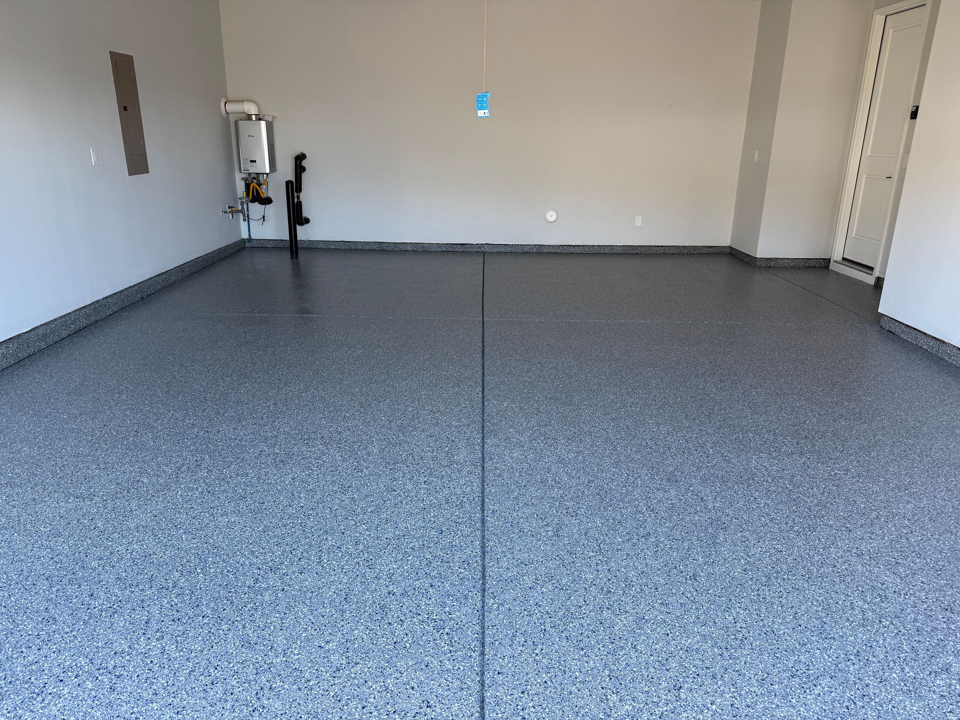 Empty garage with gray speckled floor, beige walls, and a utility area on the left.