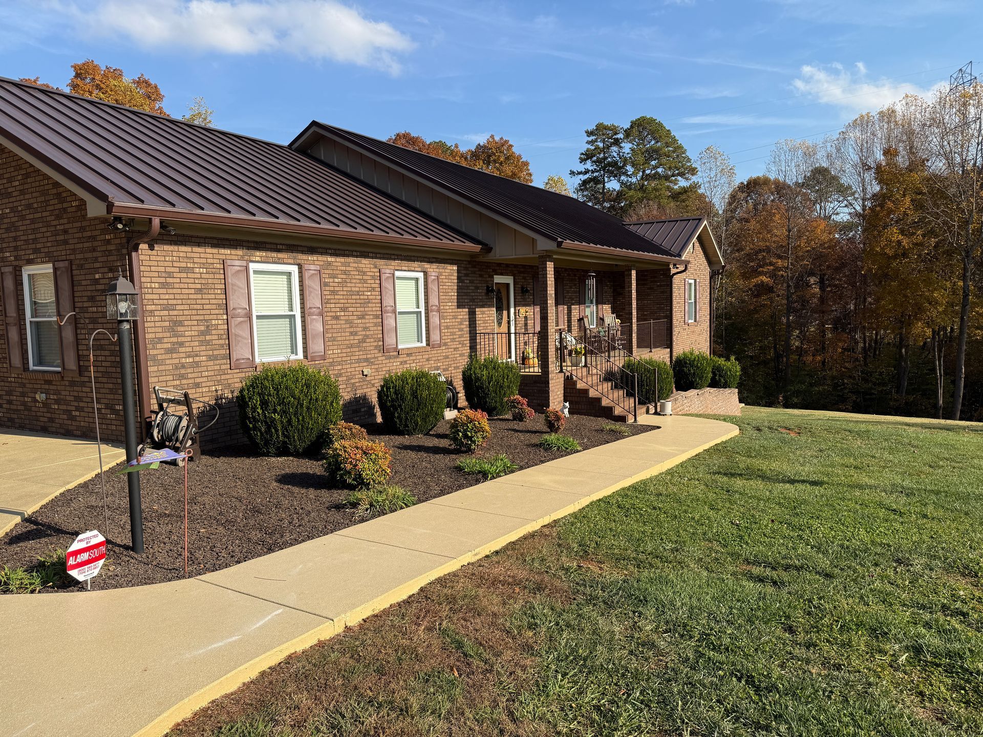 Single-story brick house with porch, walkway, and lawn under a blue sky.
