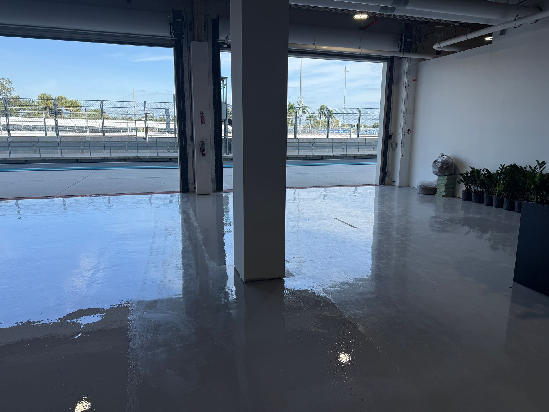 Empty industrial space with polished concrete floor and open garage doors facing an outdoor railway.
