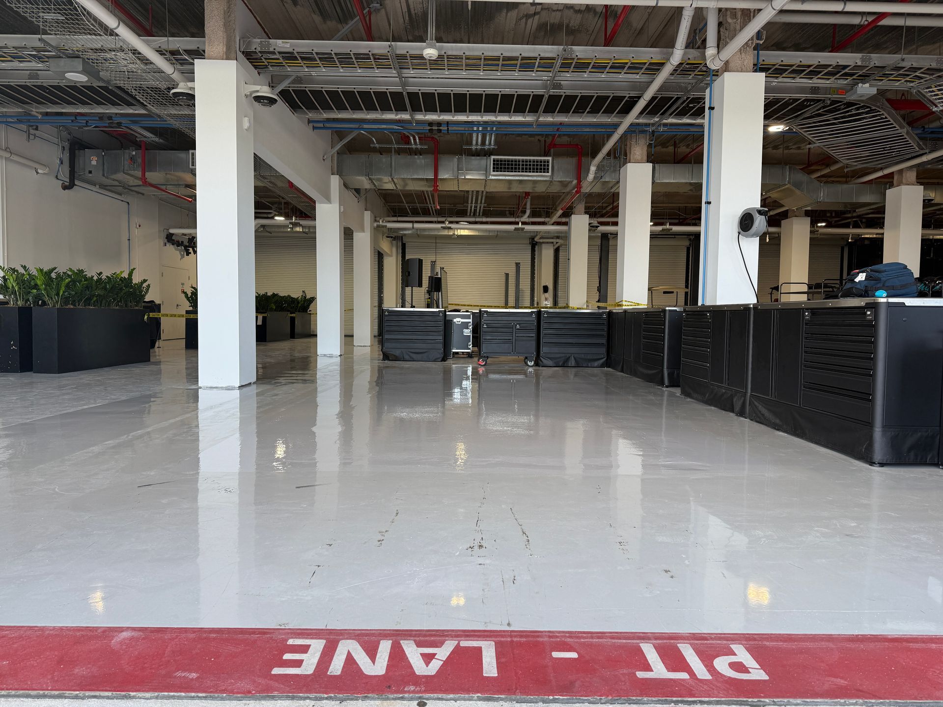 Empty industrial interior with glossy white floor, black barriers, and red “PIT LANE” marking in foreground