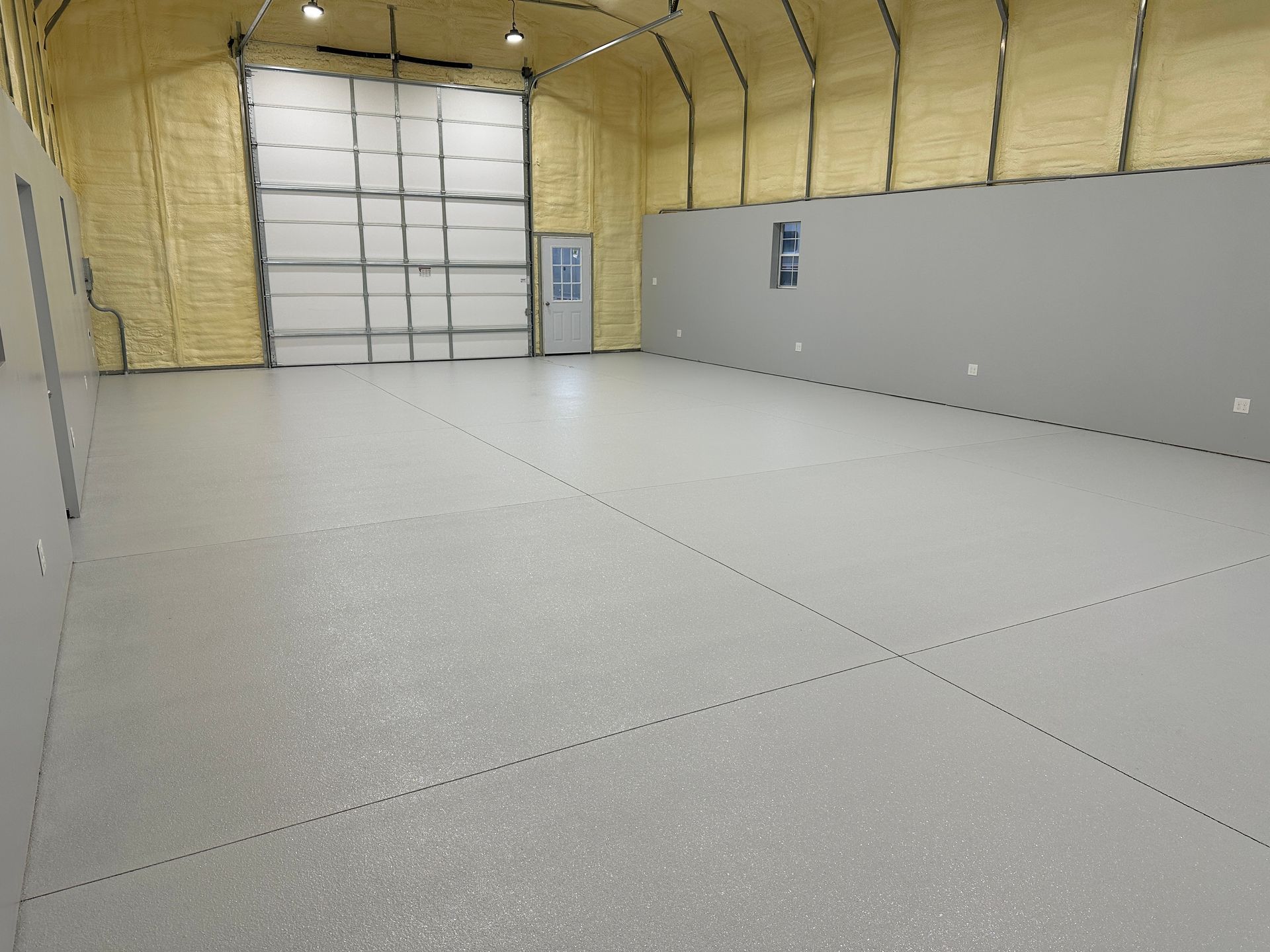 Empty insulated warehouse interior with concrete floor, large roll-up door, and gray wall panels