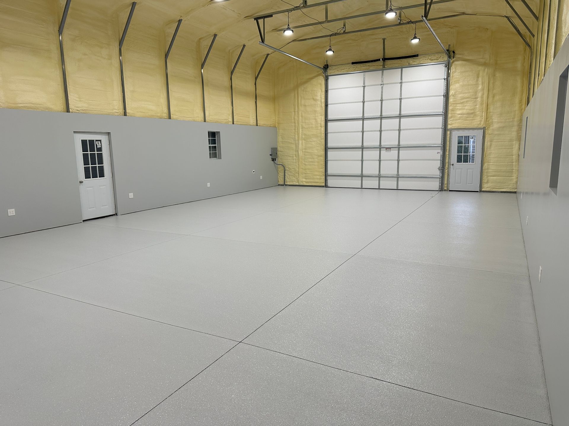 Empty insulated warehouse with white floor, gray side wall, and large overhead garage door.