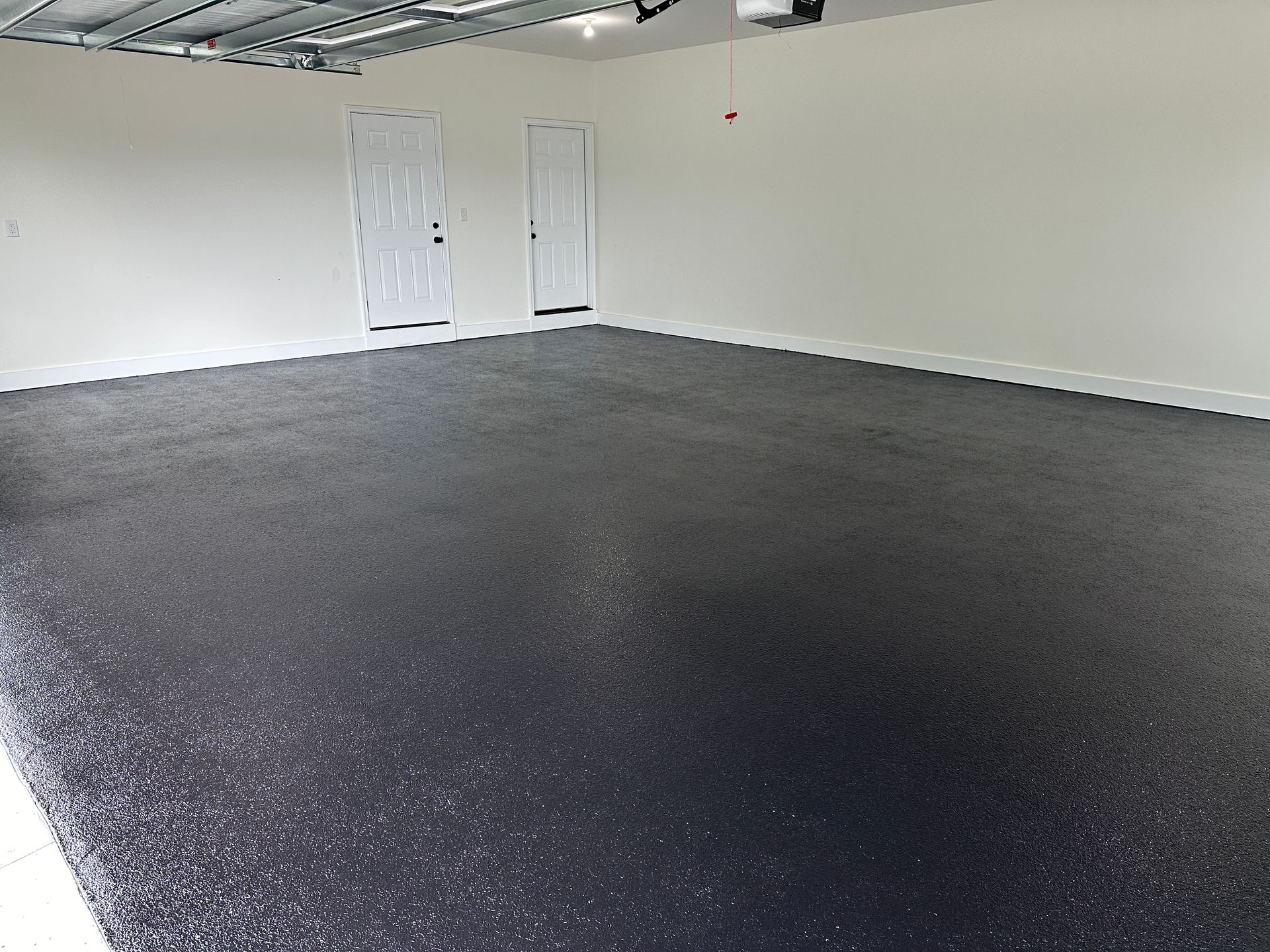 Empty garage with dark speckled floor and white walls, viewed from inside toward a closed door.