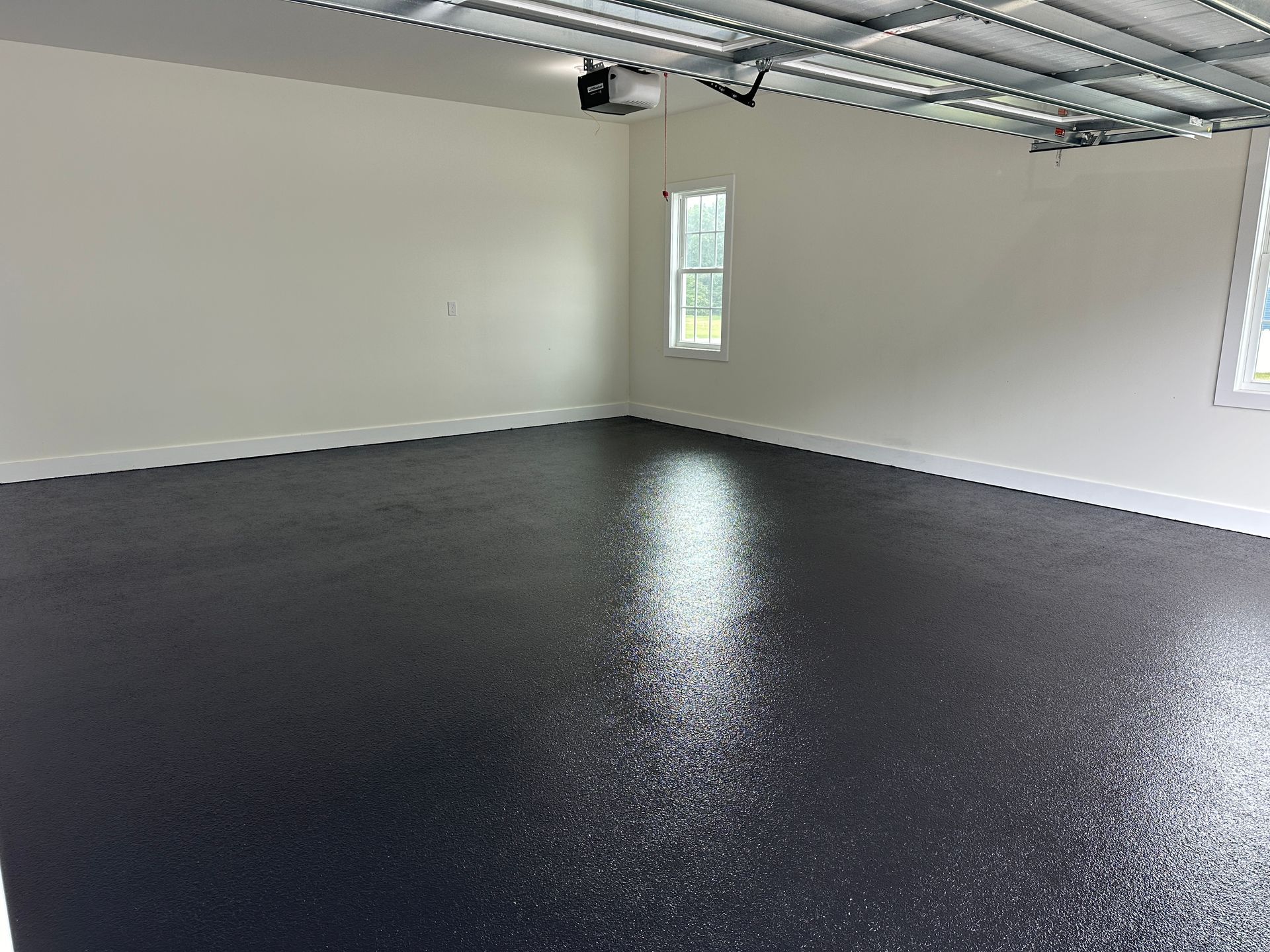 Empty garage with a glossy black floor, white walls, and a single window.