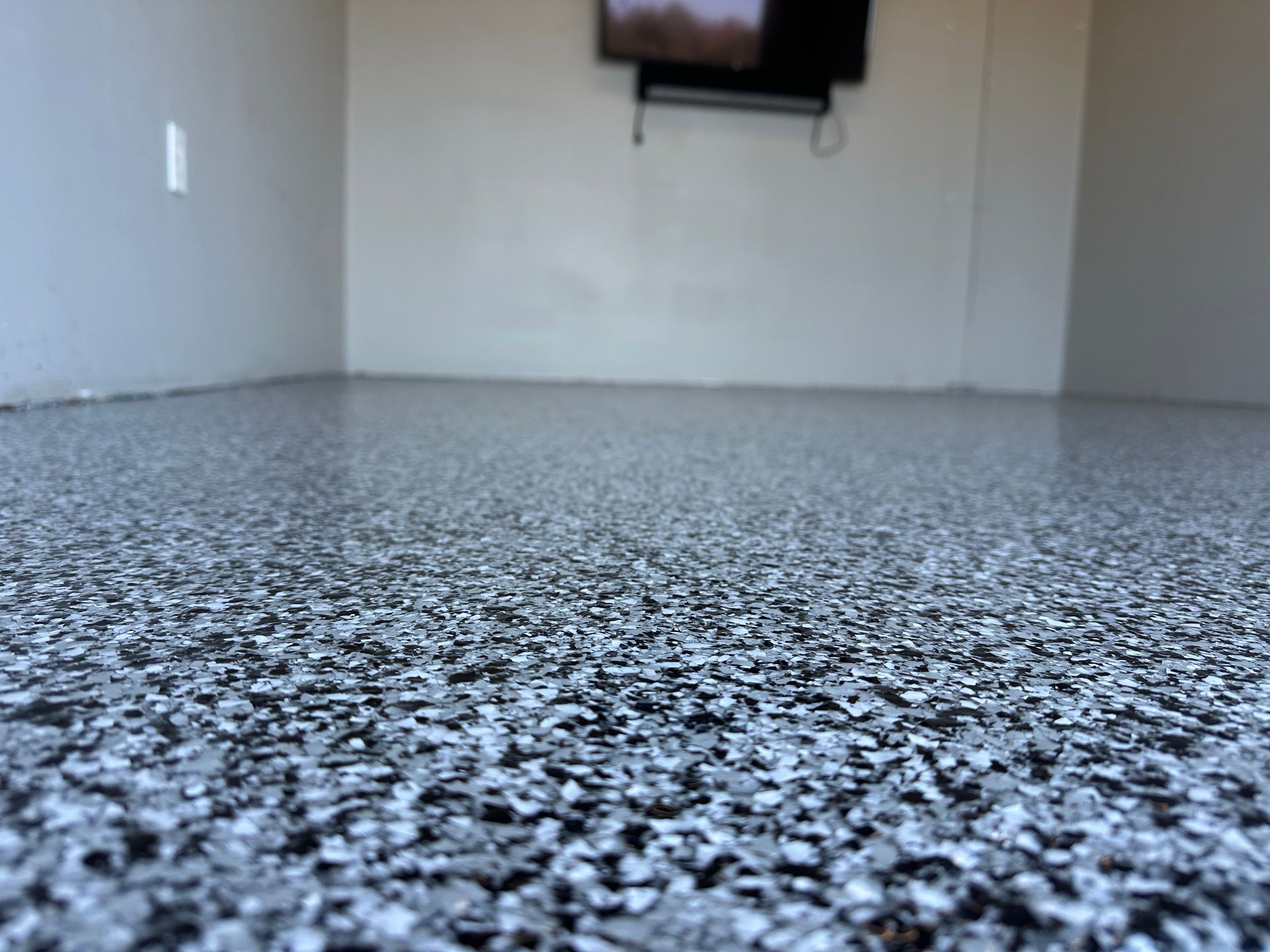 Empty room with speckled gray floor and a wall-mounted TV in the background