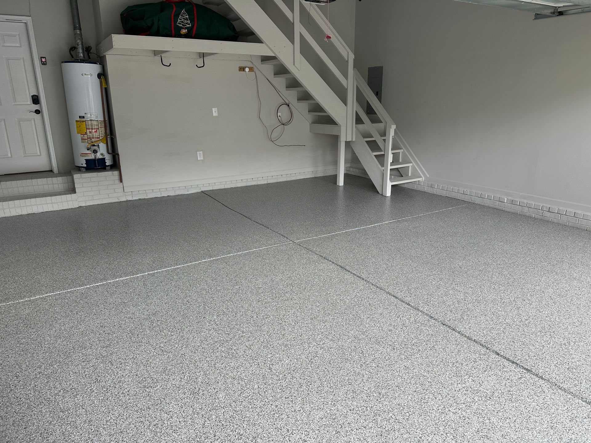 Empty garage with speckled epoxy floor, white stairs, and storage cabinets.