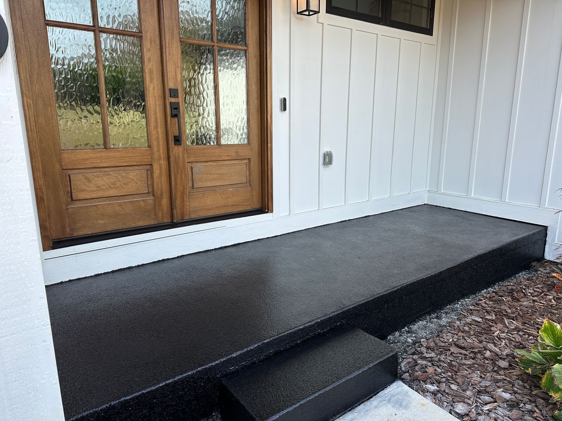 Front porch with black ramp and step beside white house and wooden door