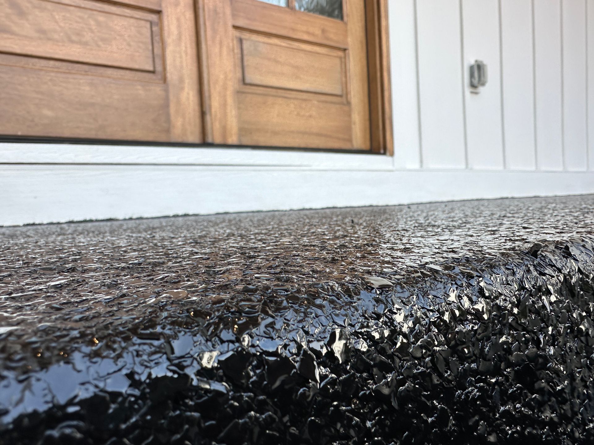 Close-up of a rough black step below wooden double doors and white siding