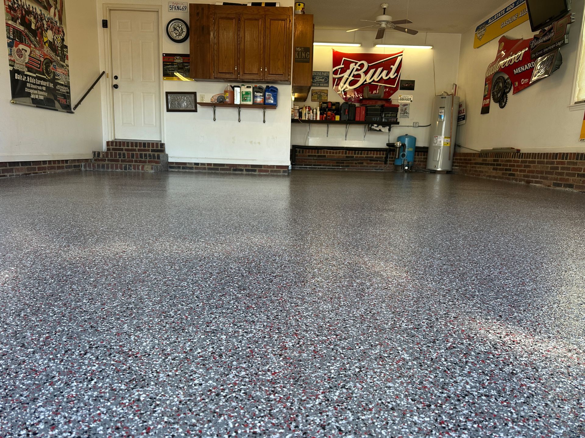 Empty garage with speckled epoxy floor, brick baseboards, cabinets, and a Budweiser sign on the back wall