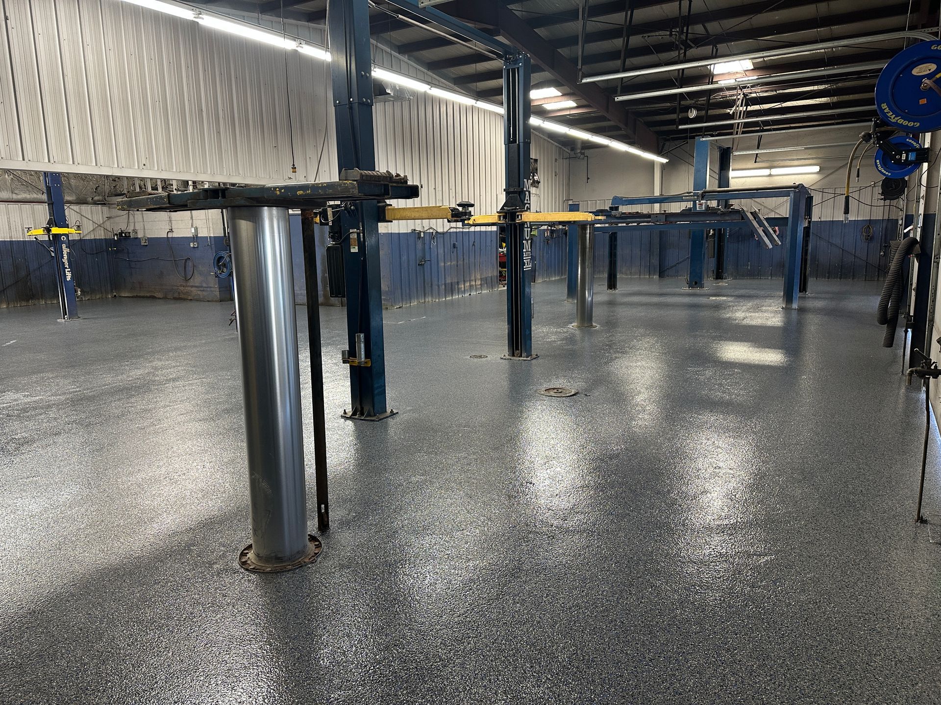 Empty industrial room with polished concrete floor, metal columns, and overhead pipes under bright lights