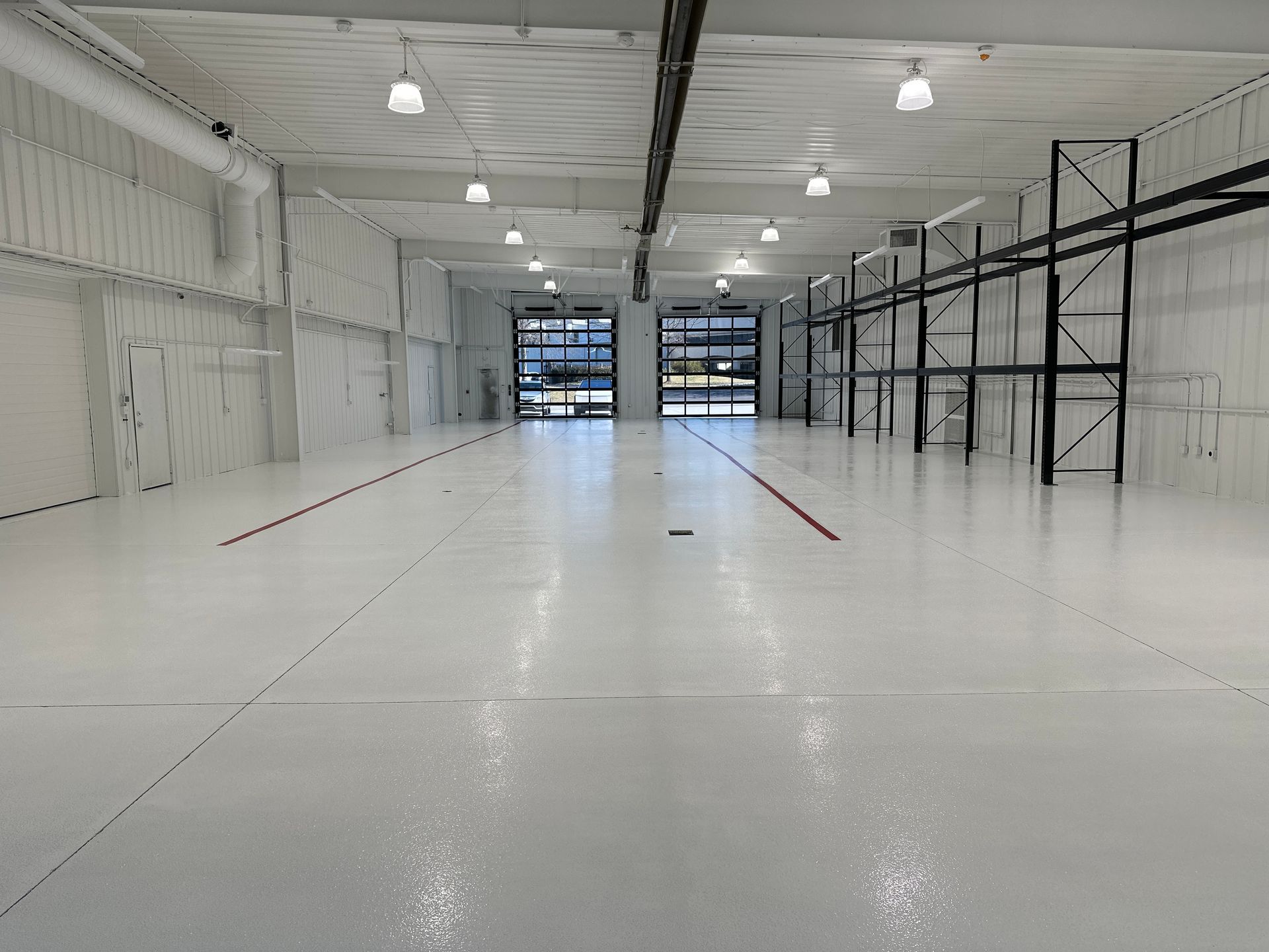 Empty white warehouse interior with polished floor and metal shelving racks along the right wall