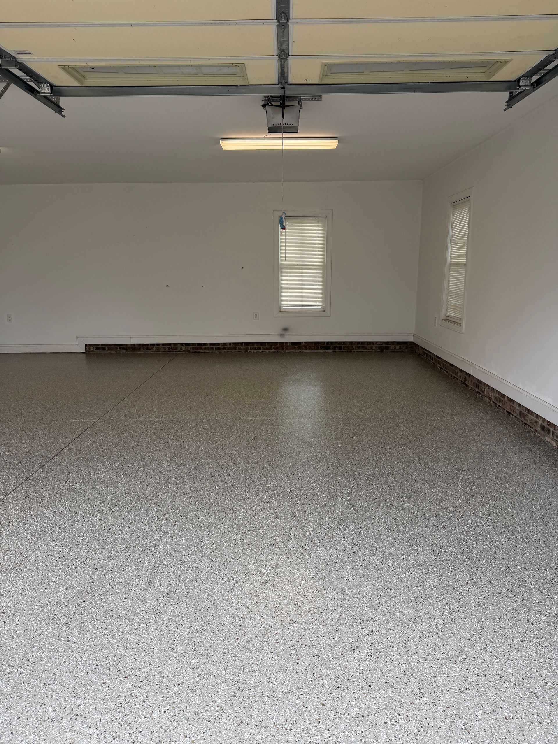 Empty white garage with speckled floor, ceiling light, and small windows.