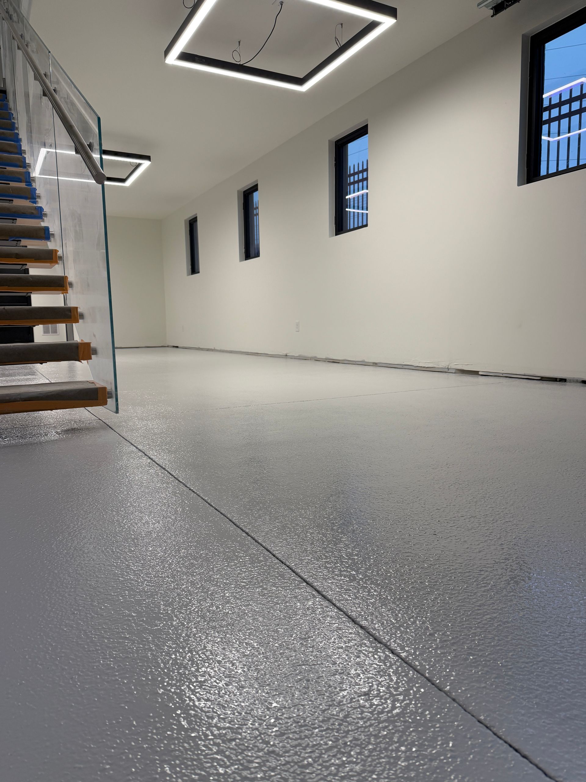 Modern interior stairwell with speckled gray floor, white walls, narrow windows, and stairs on the left
