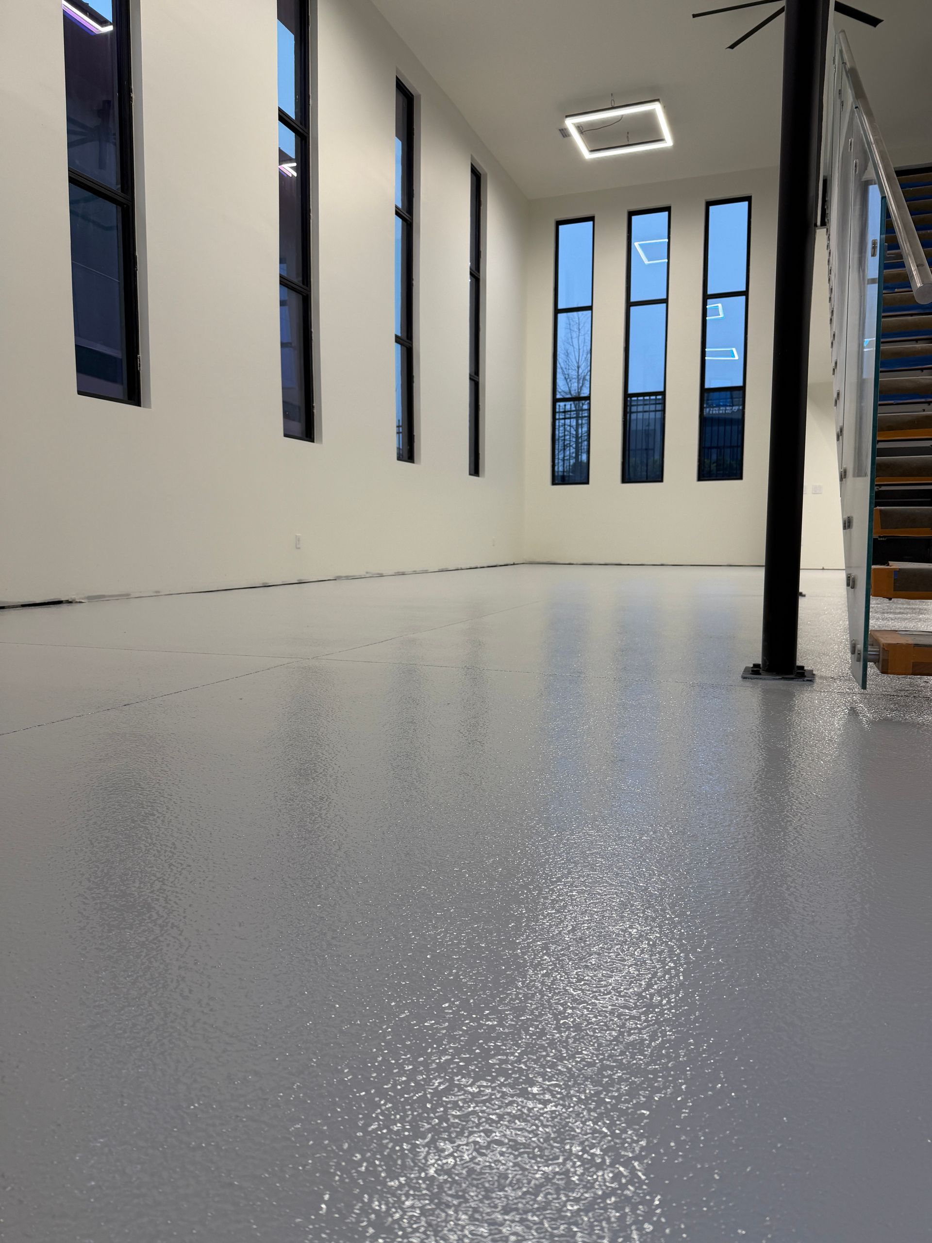 Empty modern room with glossy gray floor, tall narrow windows, white walls, and a staircase on the right