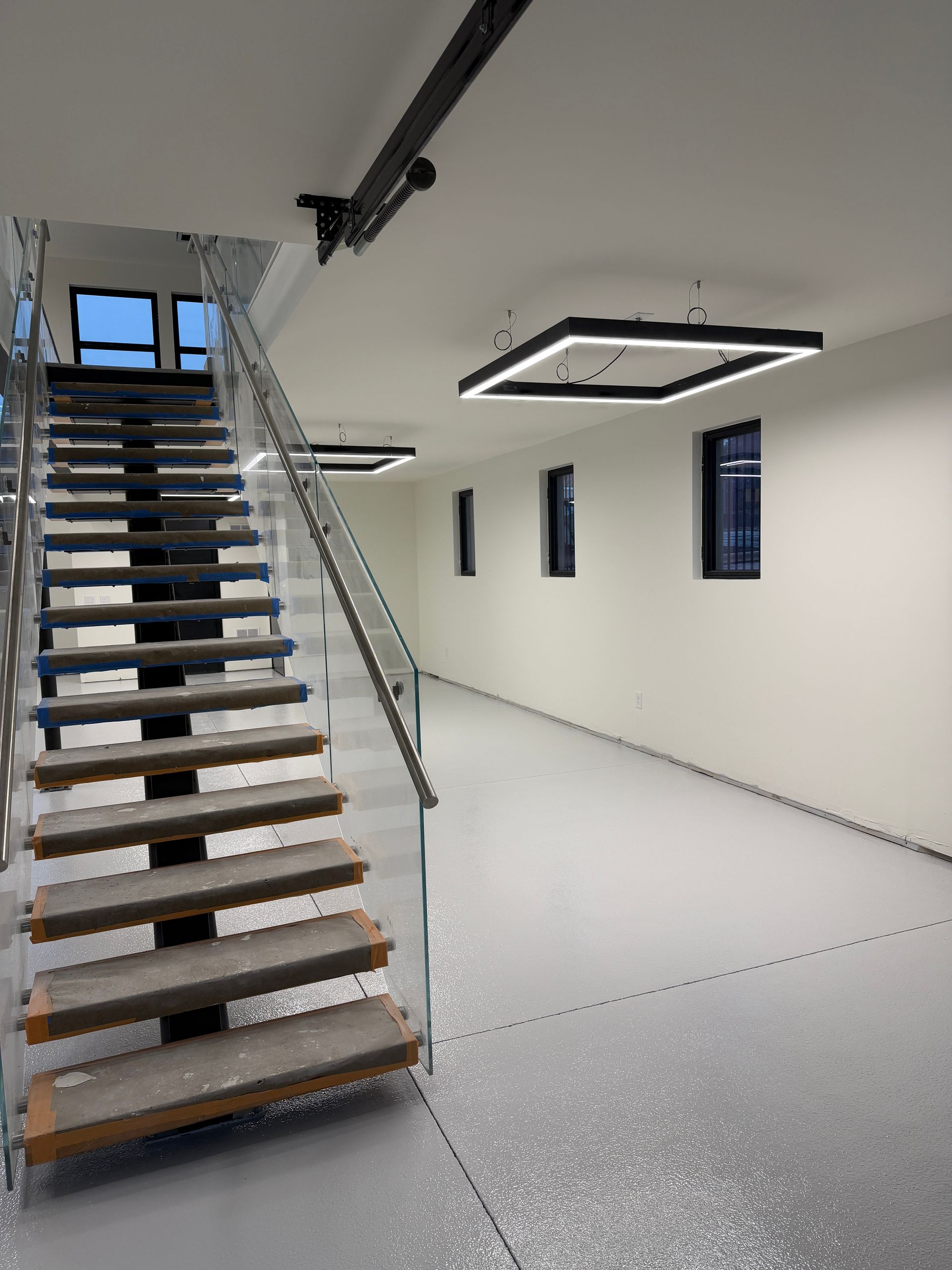 Modern stairway in a bright empty room with white walls, metal railings, and blue window frames