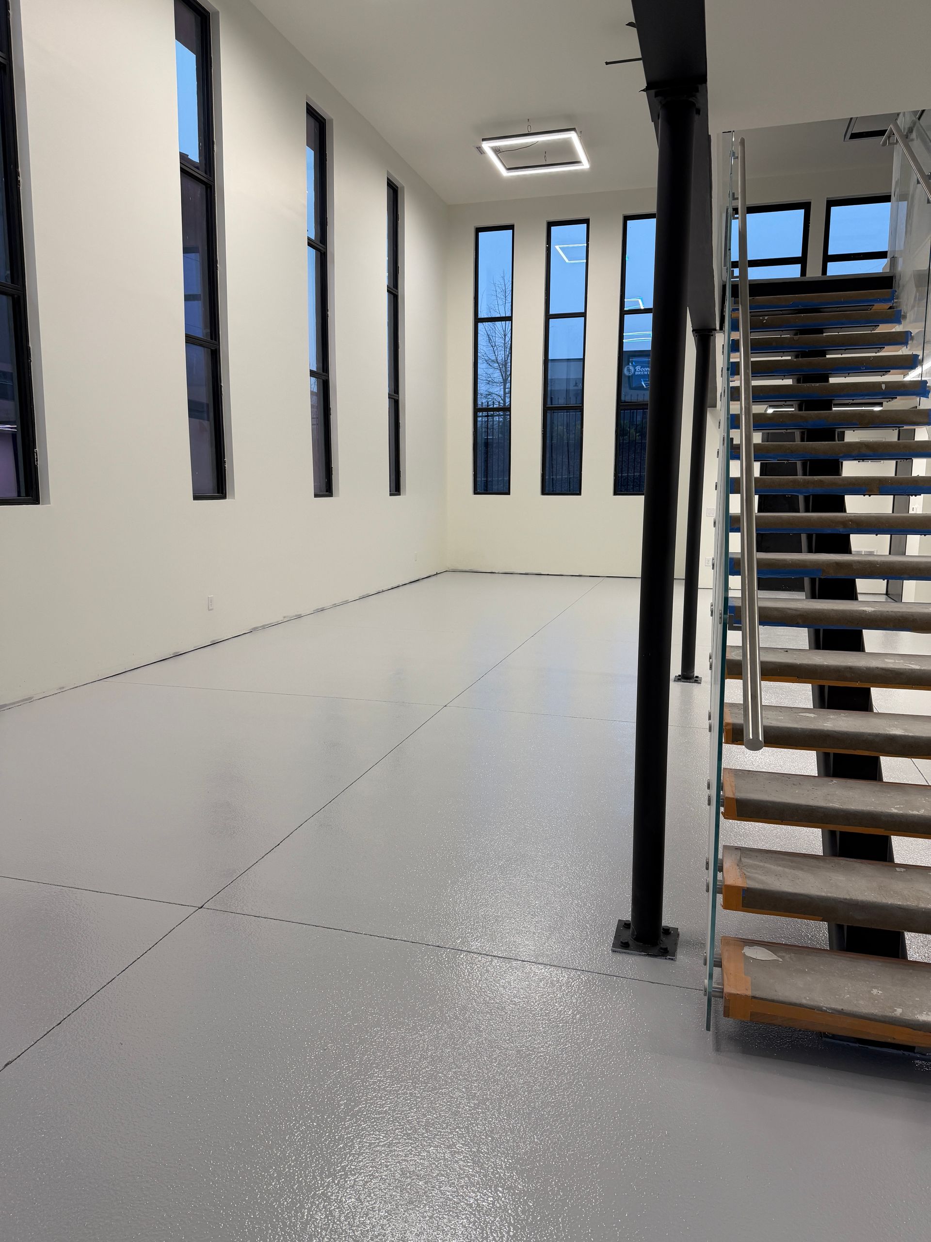 Bright empty interior with white floors, tall narrow windows, and a staircase on the right.