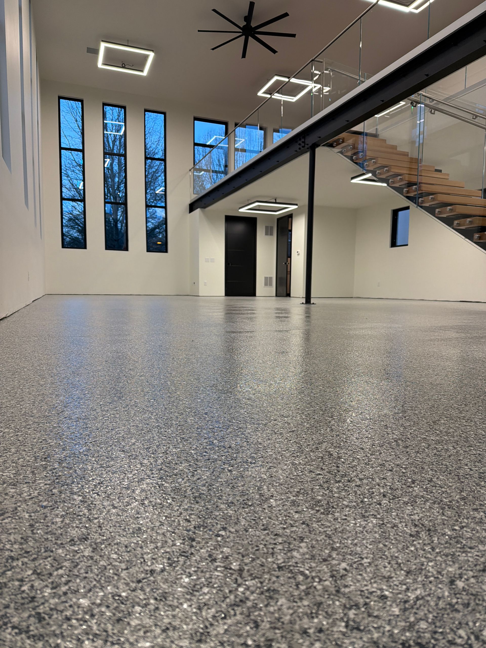 Modern lobby with speckled floor, tall windows, pendant lights, and a staircase on the right