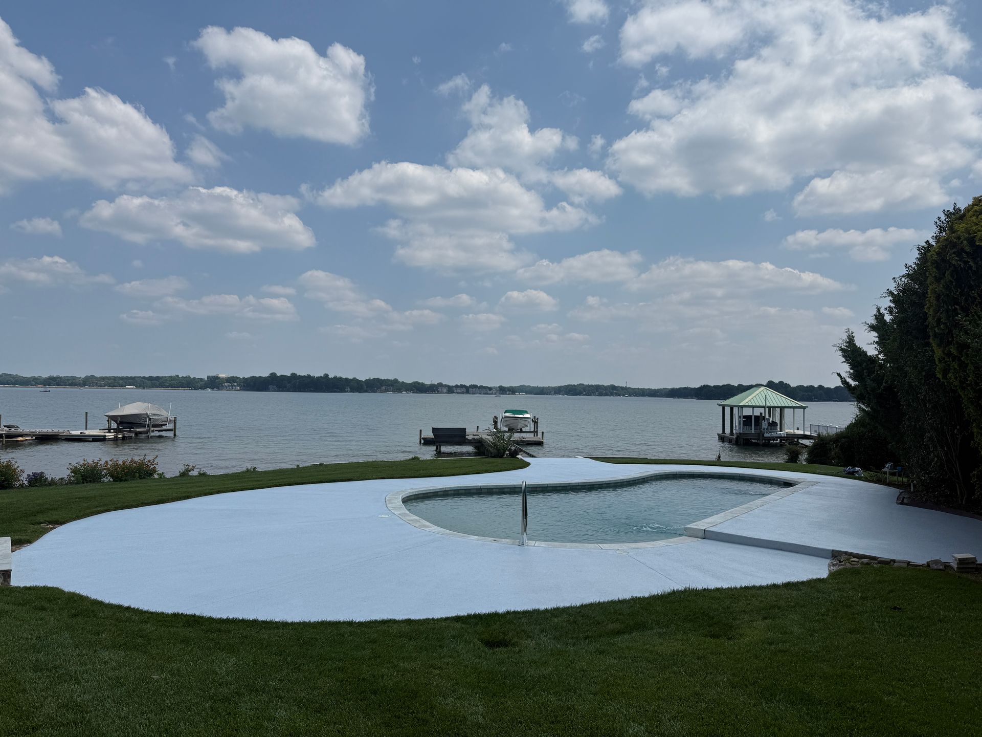 Lakeside patio with a circular blue pool, docks, and boats under a cloudy sky