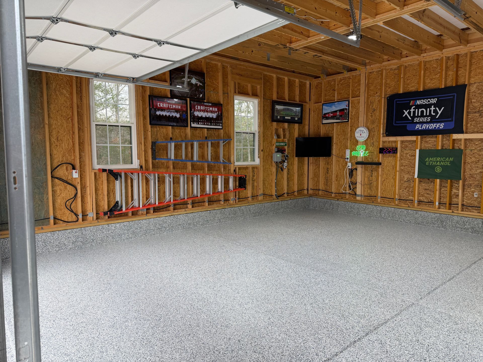 Empty wooden garage with gray floor, wall signs, shelves, and a small green figure near the right wall