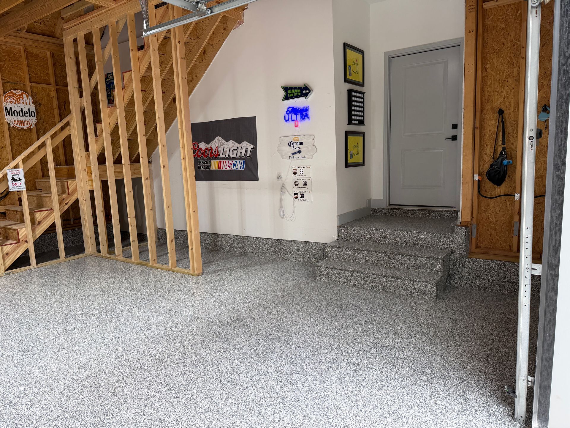 Garage interior with unfinished wooden stairs, speckled floor, and a gray door in the back wall