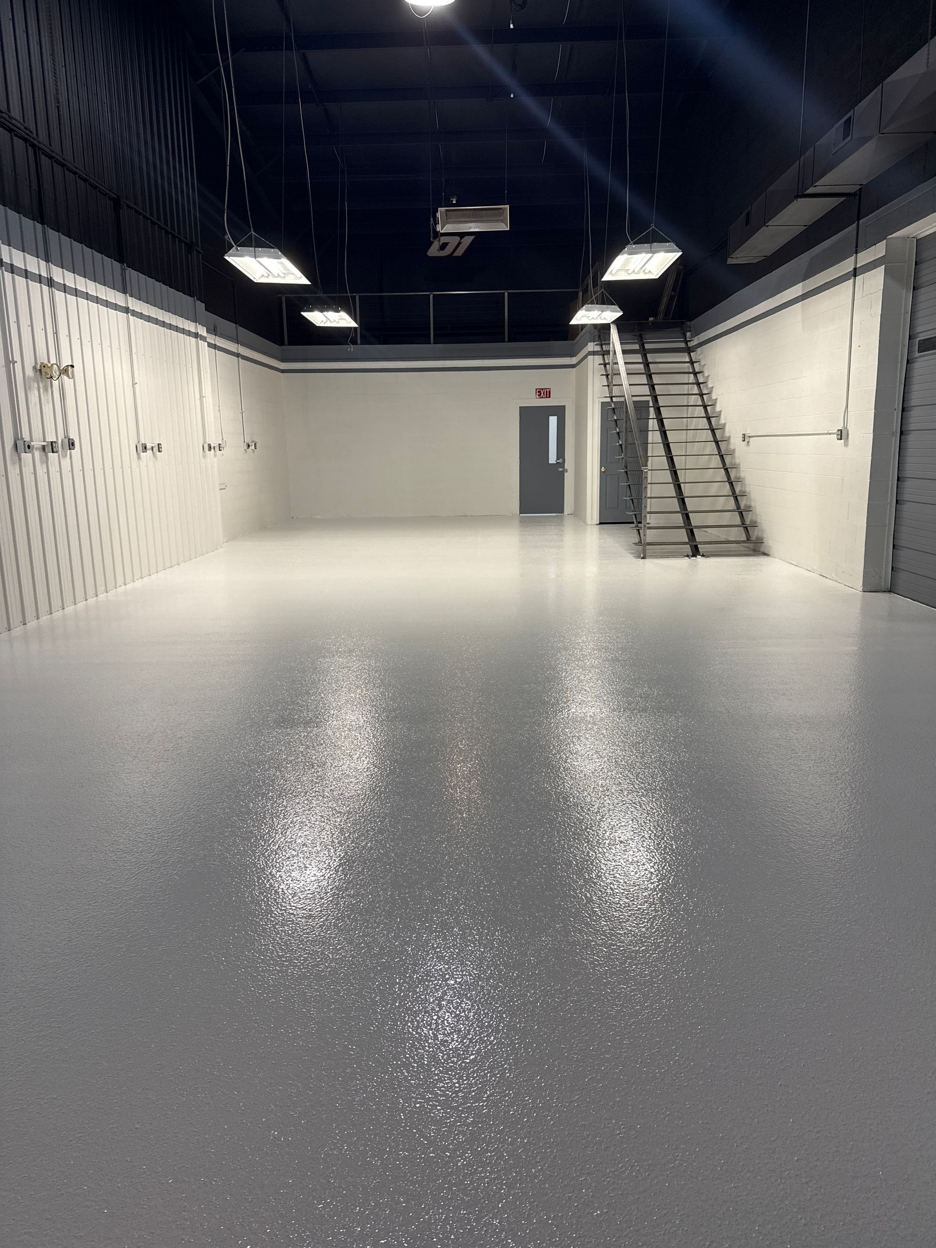 Empty white room with glossy speckled floor, black ceiling, and a small staircase at the back right.
