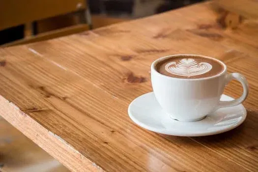 White coffee cup with latte art on a saucer sits on a wooden table.
