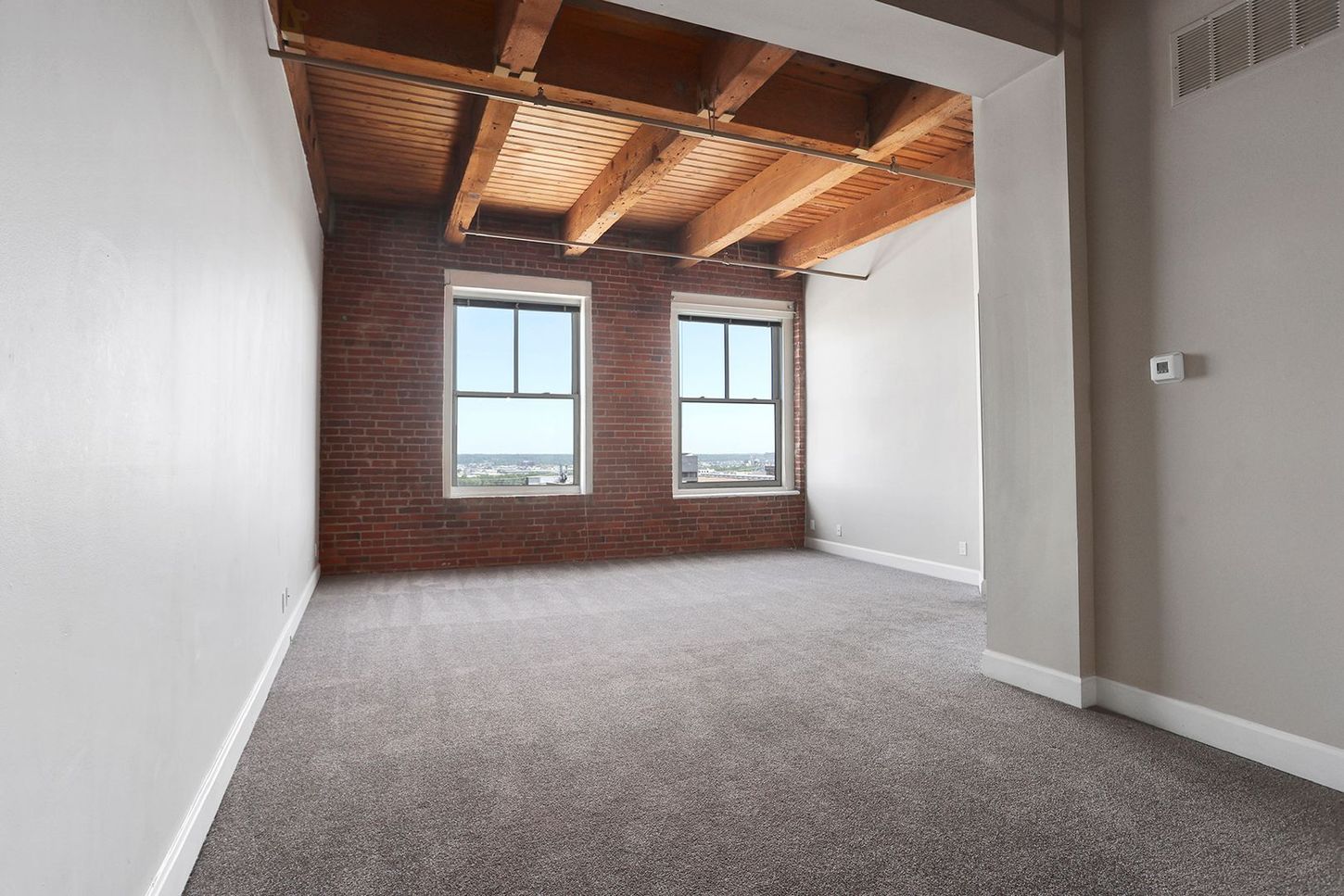 An empty room with a brick wall and two windows.
