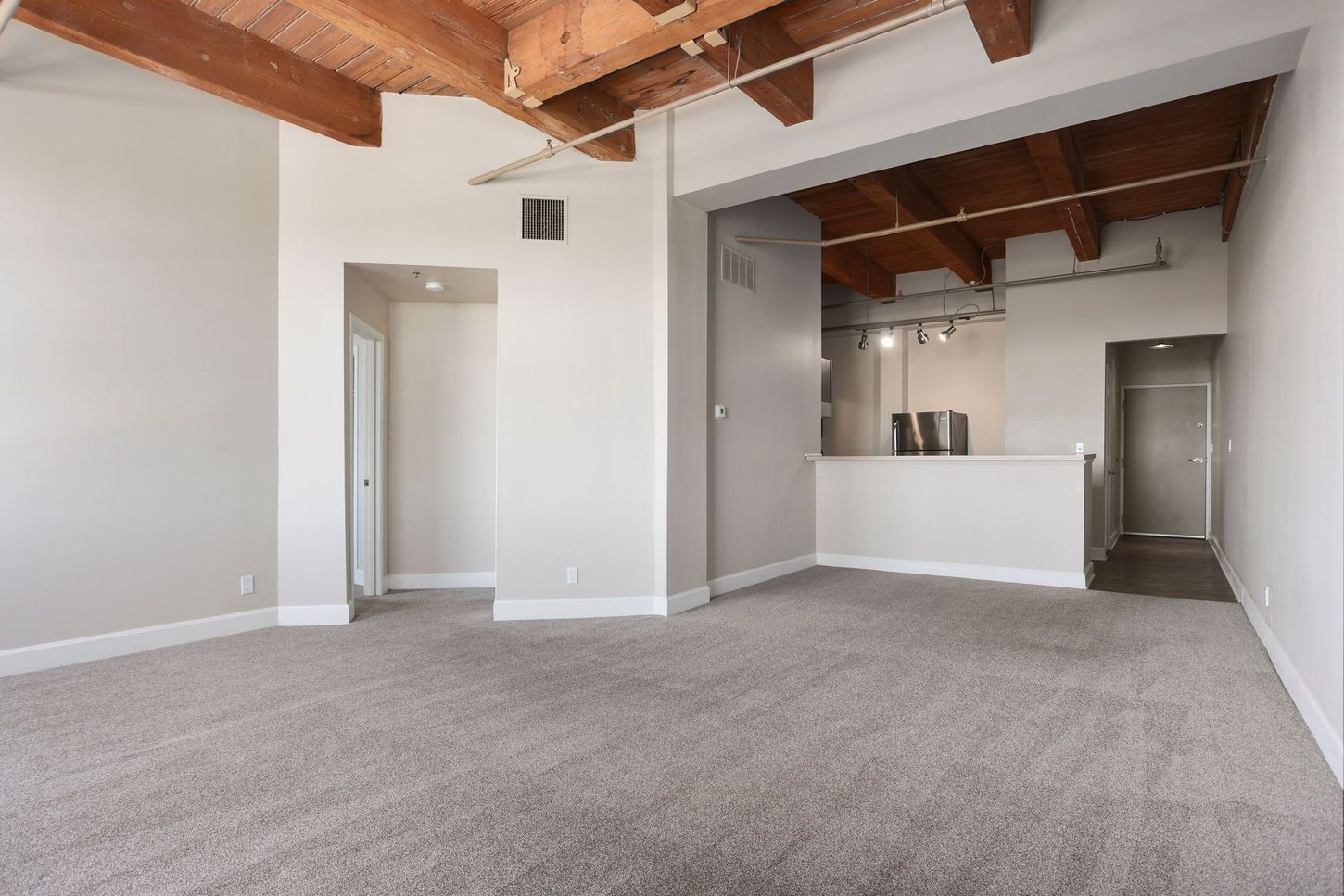 An empty living room with a carpeted floor and wooden beams
