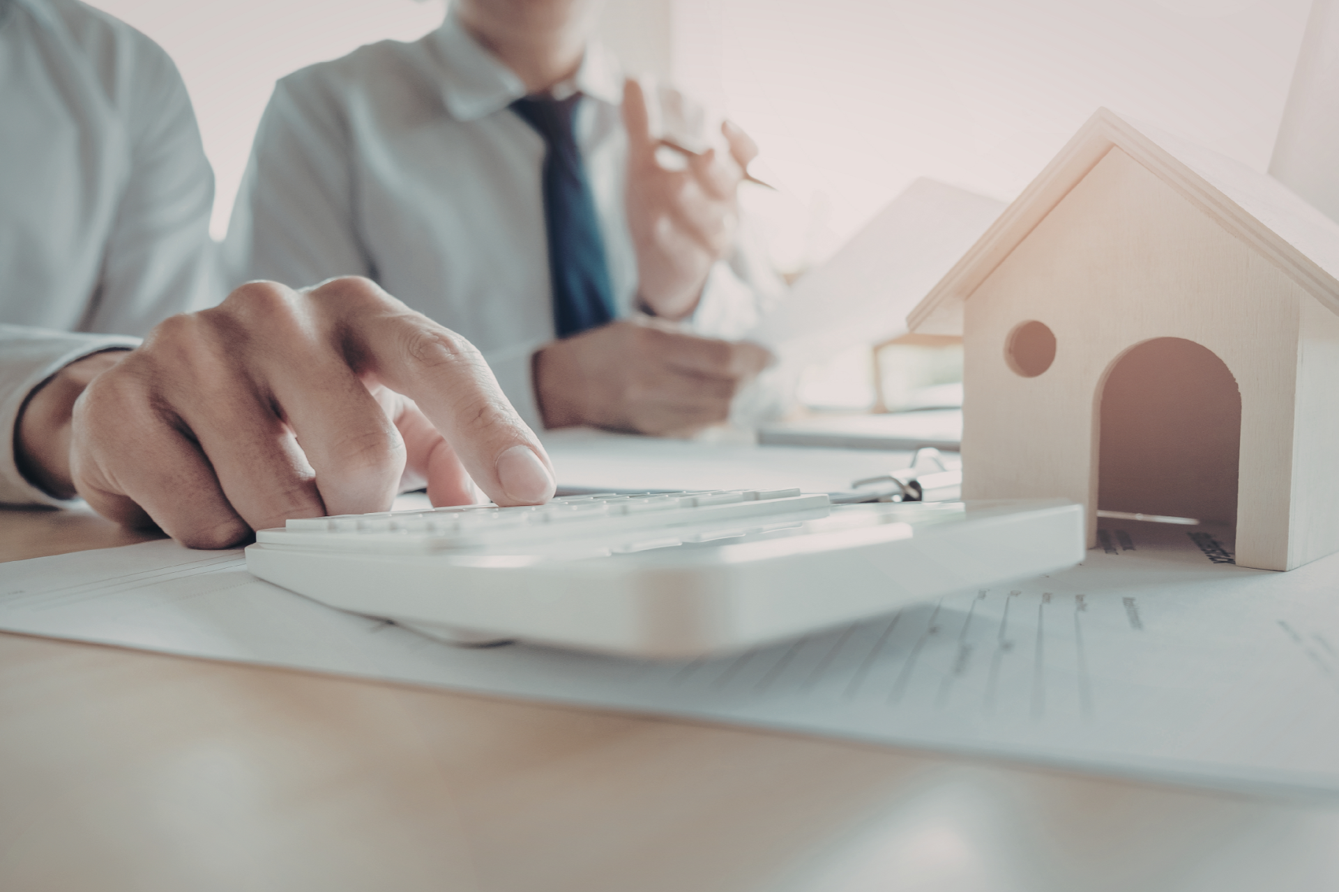 Hands reviewing house plans beside a small model home on a desk