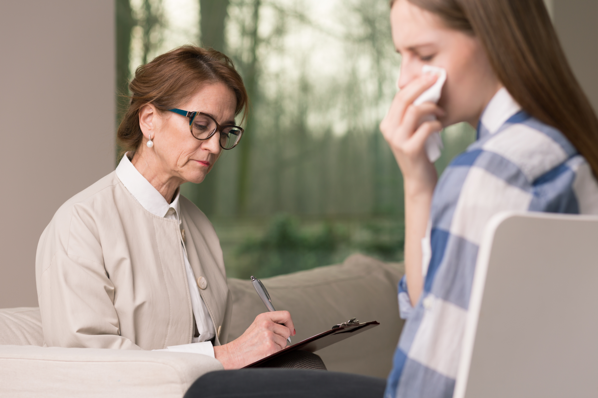 Therapist taking notes while speaking with a client in a quiet office meeting room