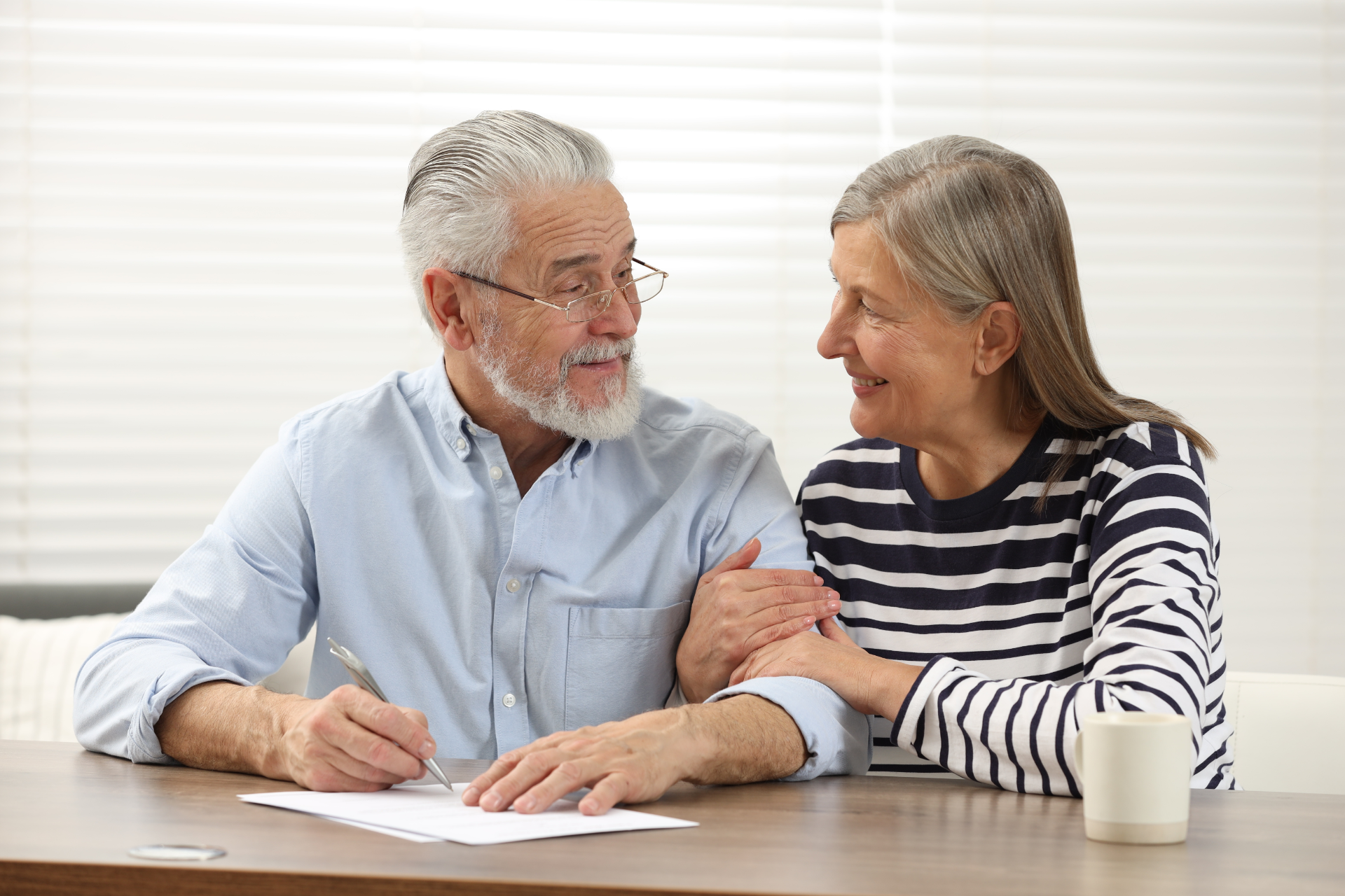 Two people smiling at a table while reviewing papers, one writing with a pen.