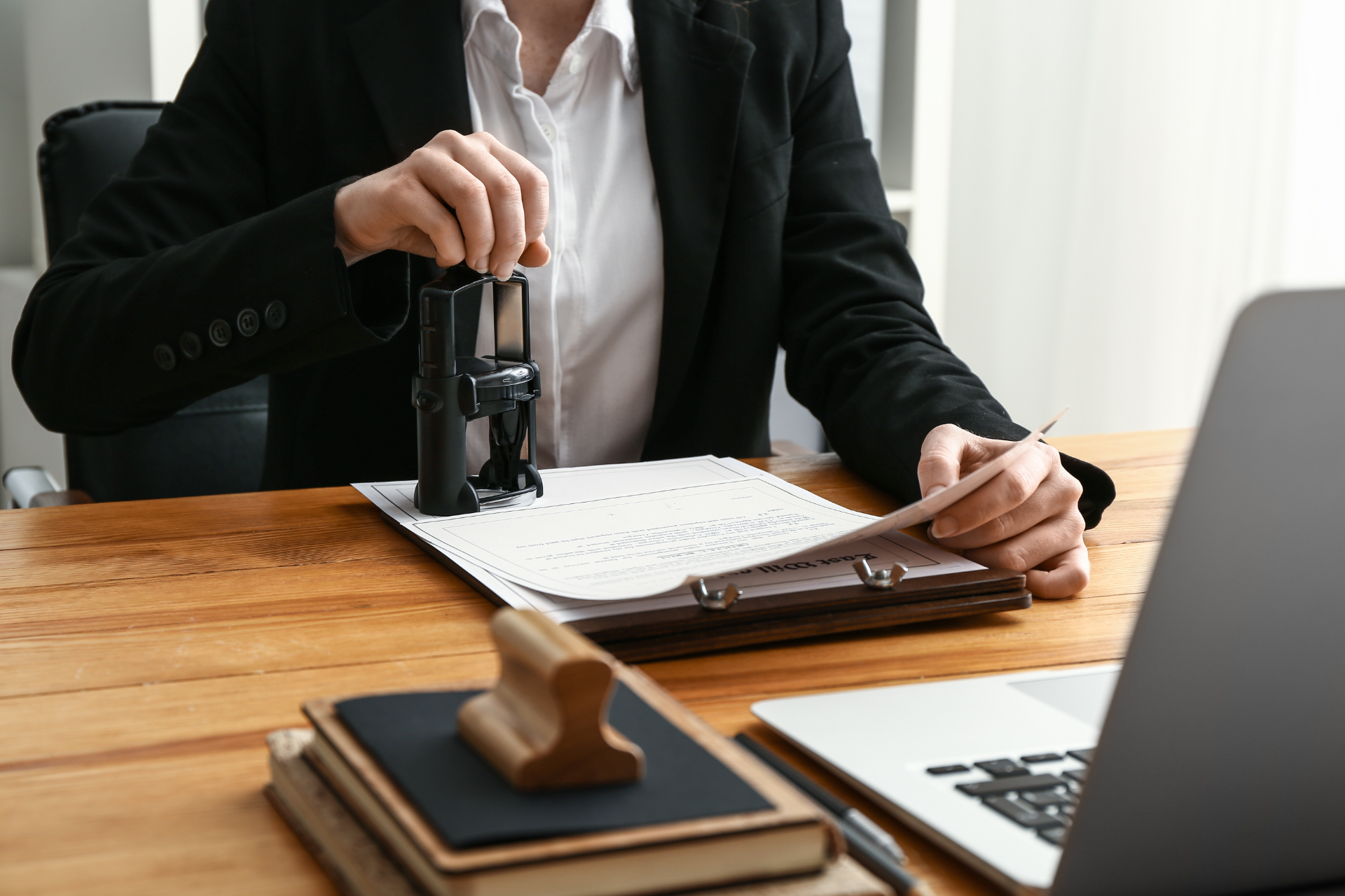 Person stamping paperwork at a desk beside a laptop and gavel, in an office setting