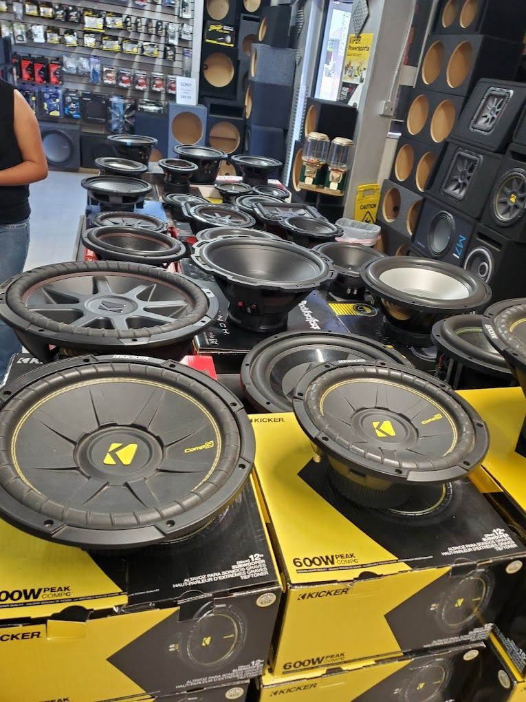 A display of car subwoofers in a store. Many black and yellow speakers are on display, some in boxes.