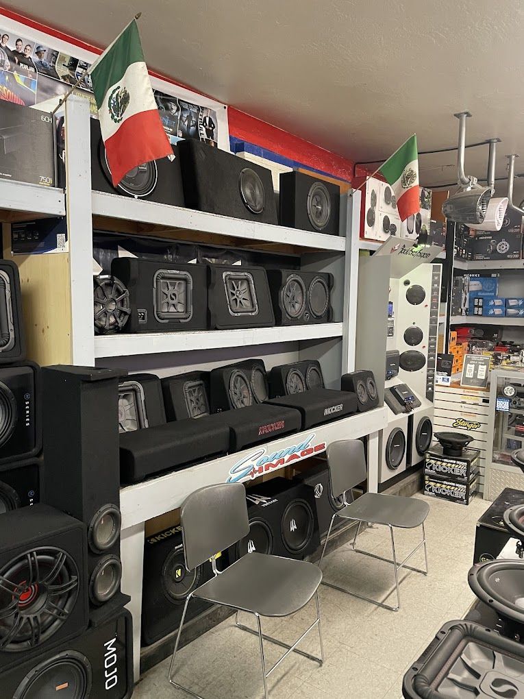 Interior of an audio shop with shelves of car subwoofers. Two Mexican flags hang from the ceiling.