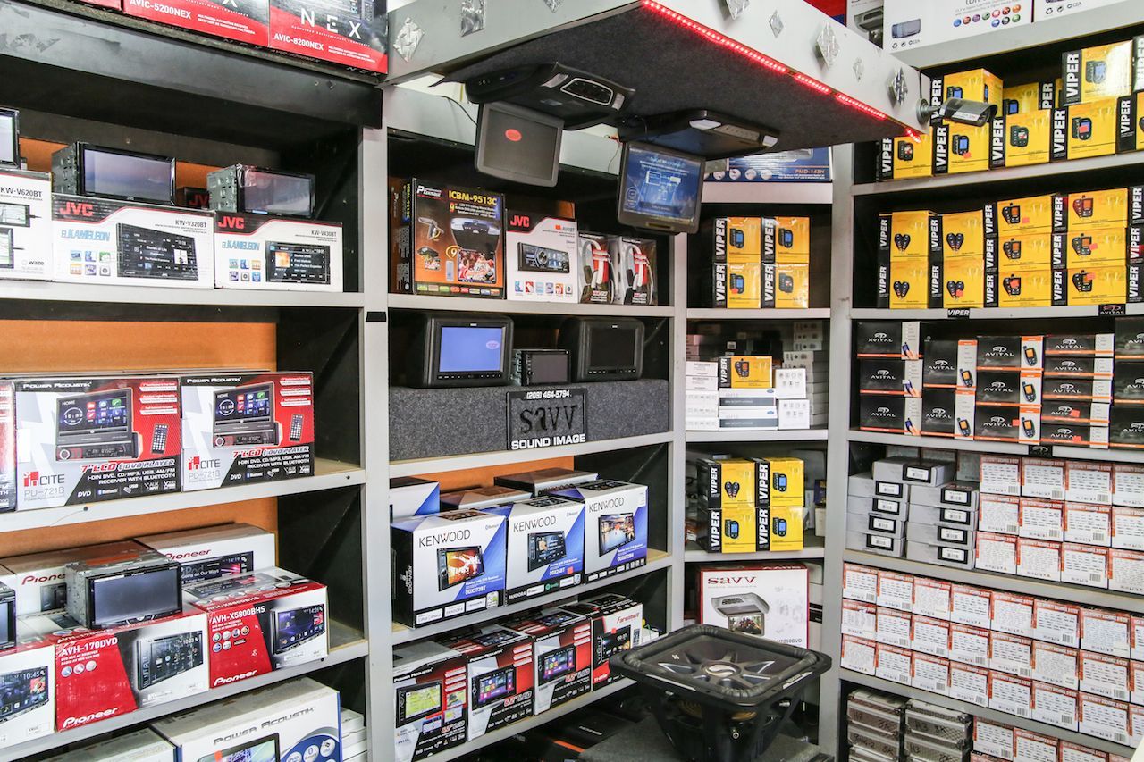Shelves stocked with car audio equipment in a retail store. Radios, speakers, and related products are visible.