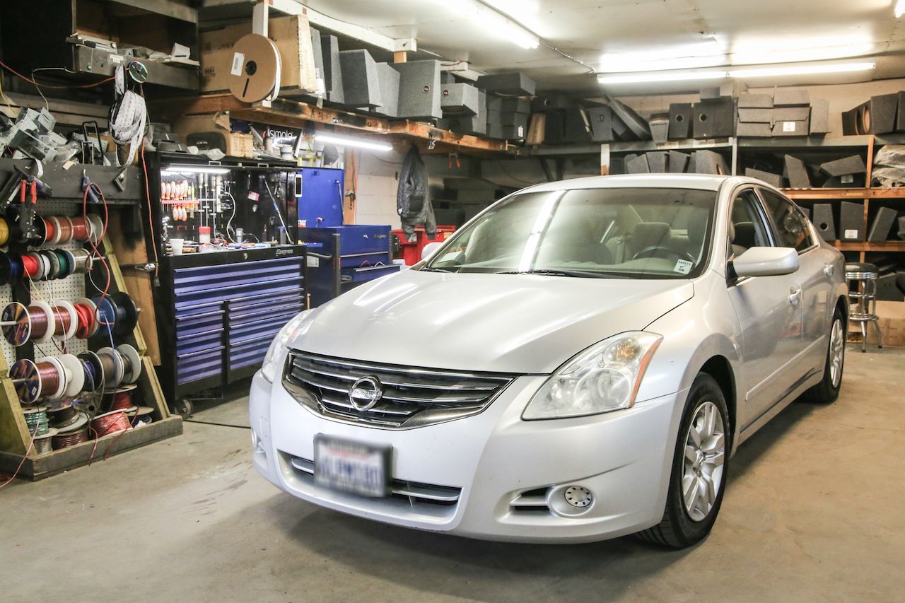 Silver Nissan Altima in a cluttered auto repair shop, with tools and parts visible.