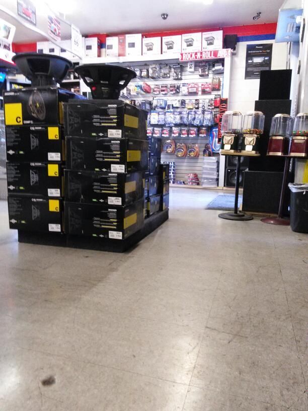 A car audio store interior. Speakers and boxes on display in front. Shelves stocked with car audio components.