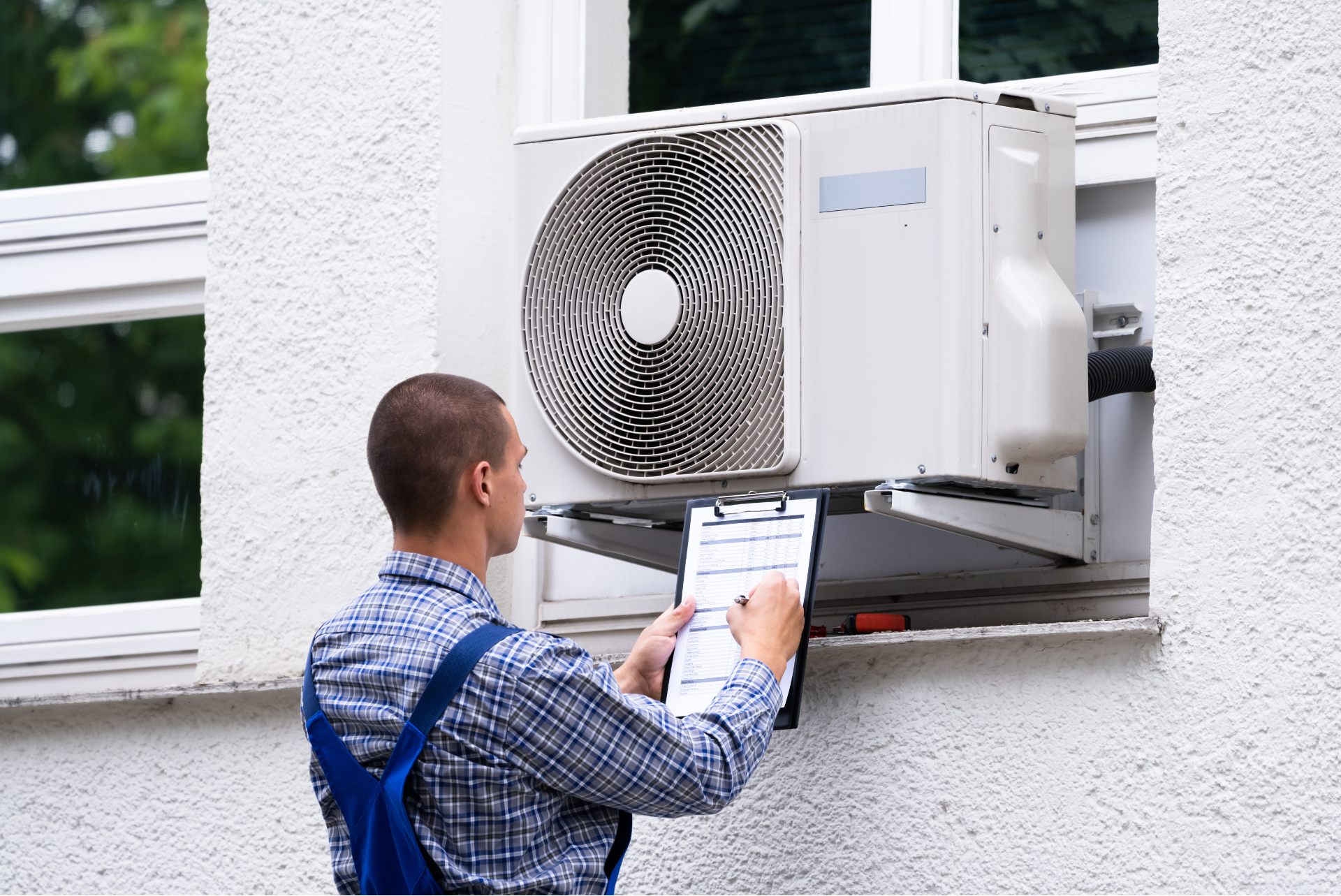 A man is holding a clipboard in front of an air conditioner.