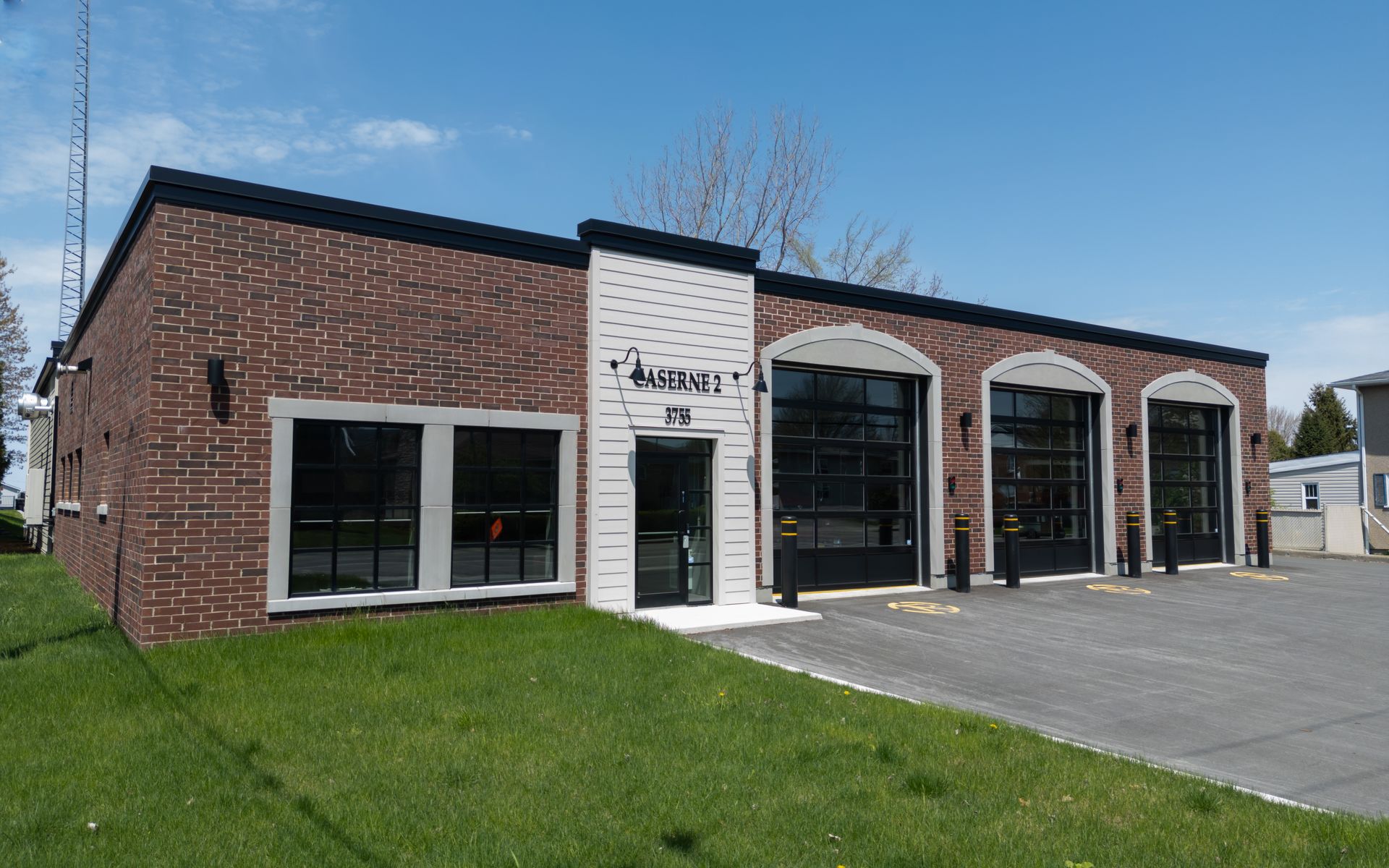 Atelier de réparation automobile en briques, avec de grandes portes de garage et une allée pavée sous un ciel bleu.