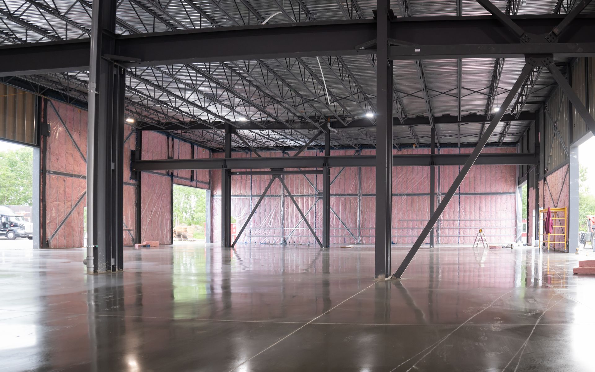 Intérieur d'un entrepôt industriel vide, avec poutres d'acier, sol en béton et toiture métallique apparente.