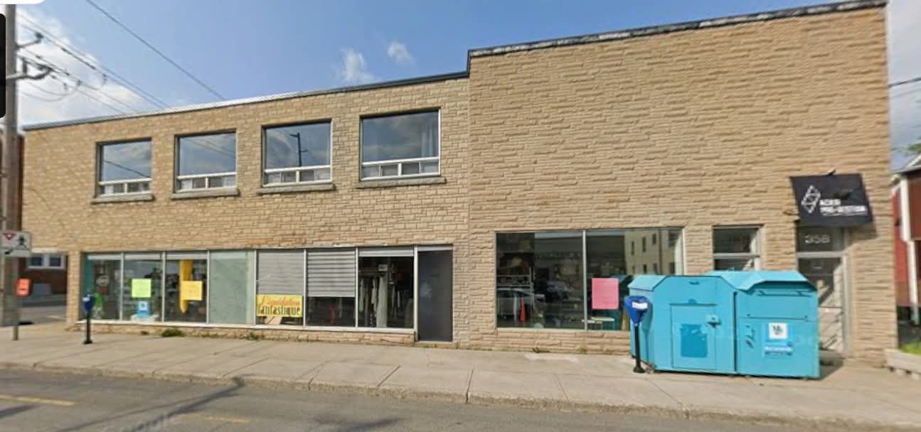 Façade commerciale en briques sur deux étages avec de grandes fenêtres et des conteneurs de recyclage bleu vif sur le trottoir