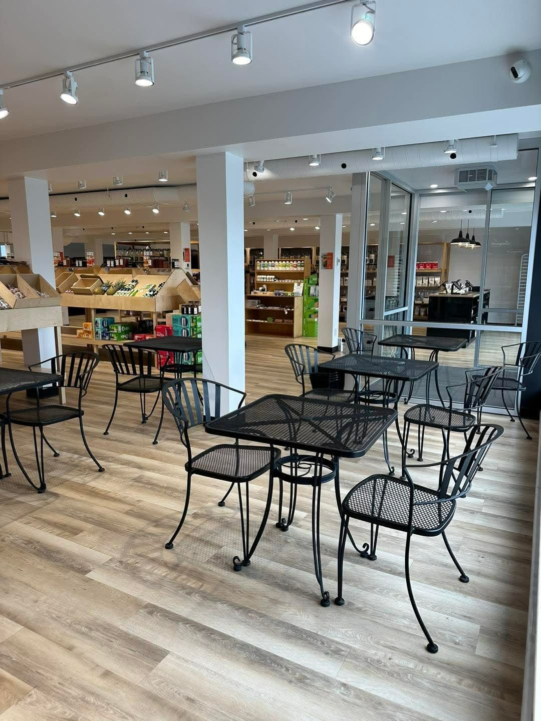 Intérieur d'un magasin avec tables et chaises en métal, sol imitation bois et présentoirs alimentaires.