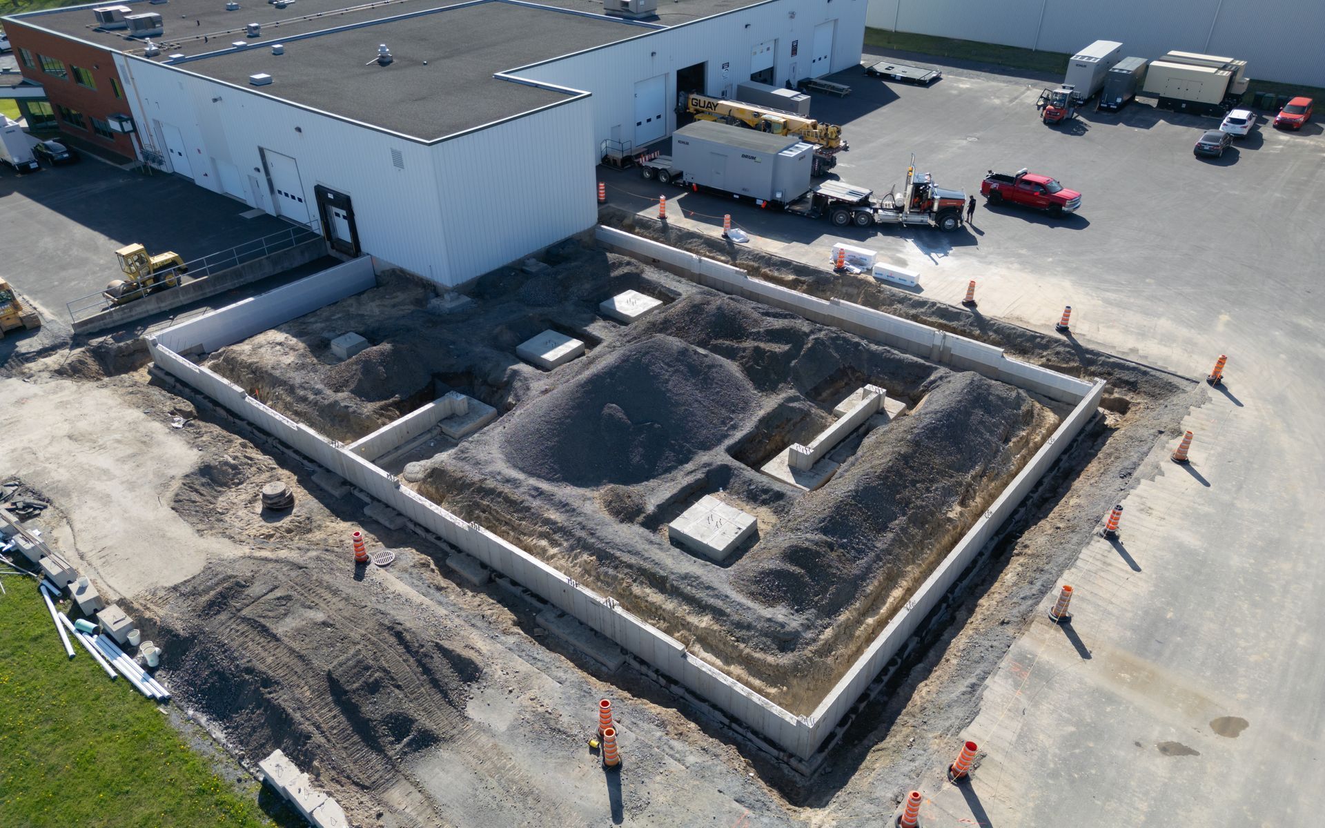 Vue aérienne d'un chantier de construction avec des murs de fondation, des tas de terre et des ouvriers près d'un entrepôt