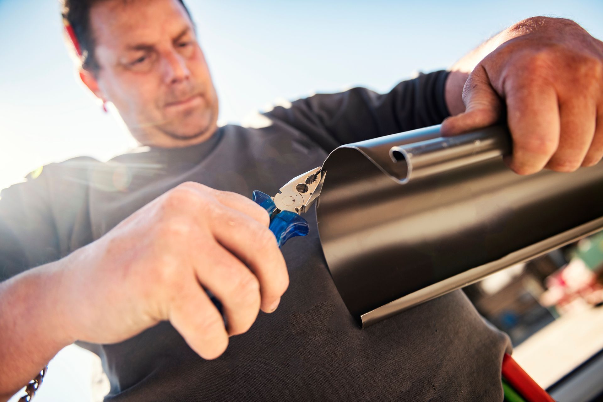 A man cutting metal with snips, illustrating a task involved in residential gutter installation.