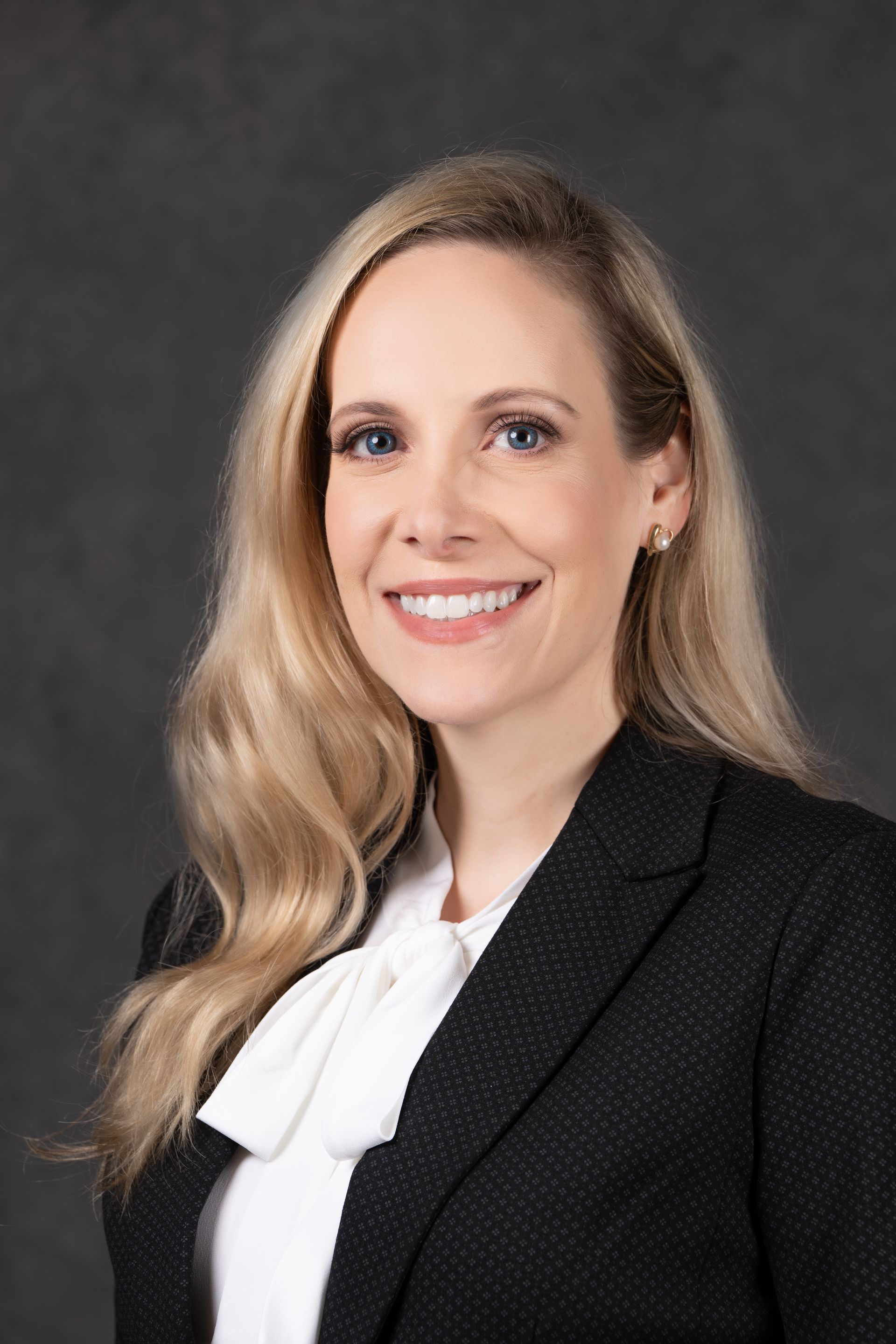 Woman with blonde hair, wearing a white blouse and black blazer, smiling at the camera.