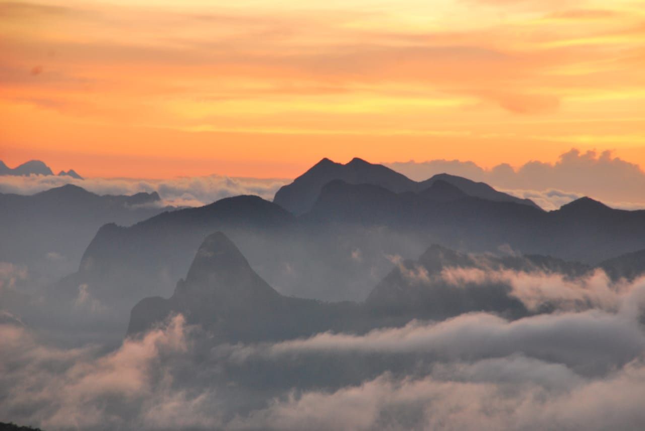 Uma paisagem deslumbrante de picos montanhosos recortados que se elevam acima de um denso mar de nuvens baixas durante um pôr do sol dourado.
