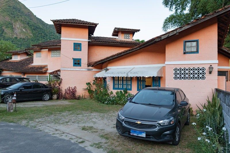 Uma casa cor de pêssego com detalhes escuros e telhado de duas águas, com dois carros estacionados em uma entrada gramada na frente.