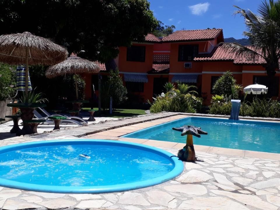 Uma área externa ensolarada com uma banheira de hidromassagem circular azul e uma piscina maior com uma fonte em formato de cogumelo.