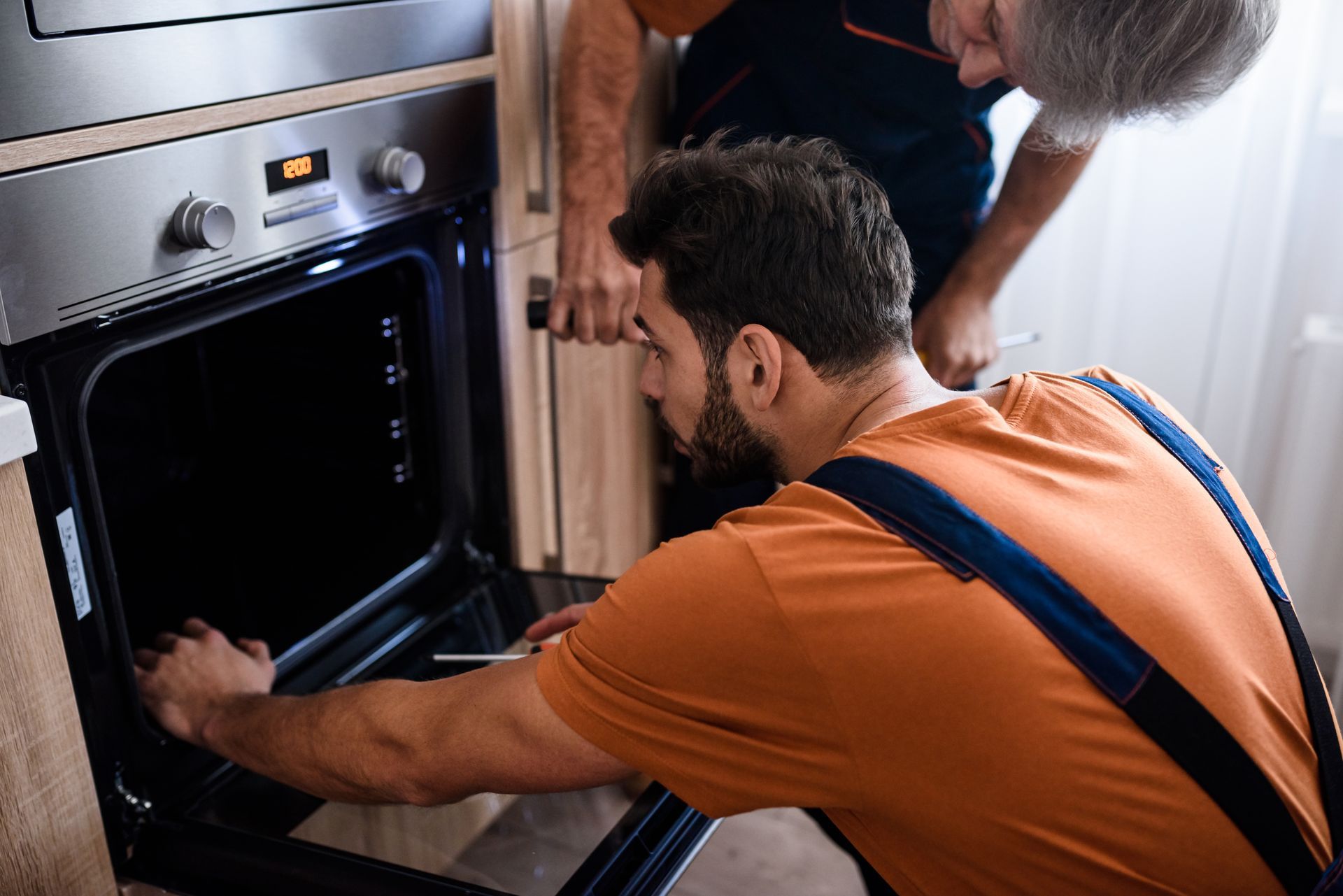 Two men are working on an oven in a kitchen.