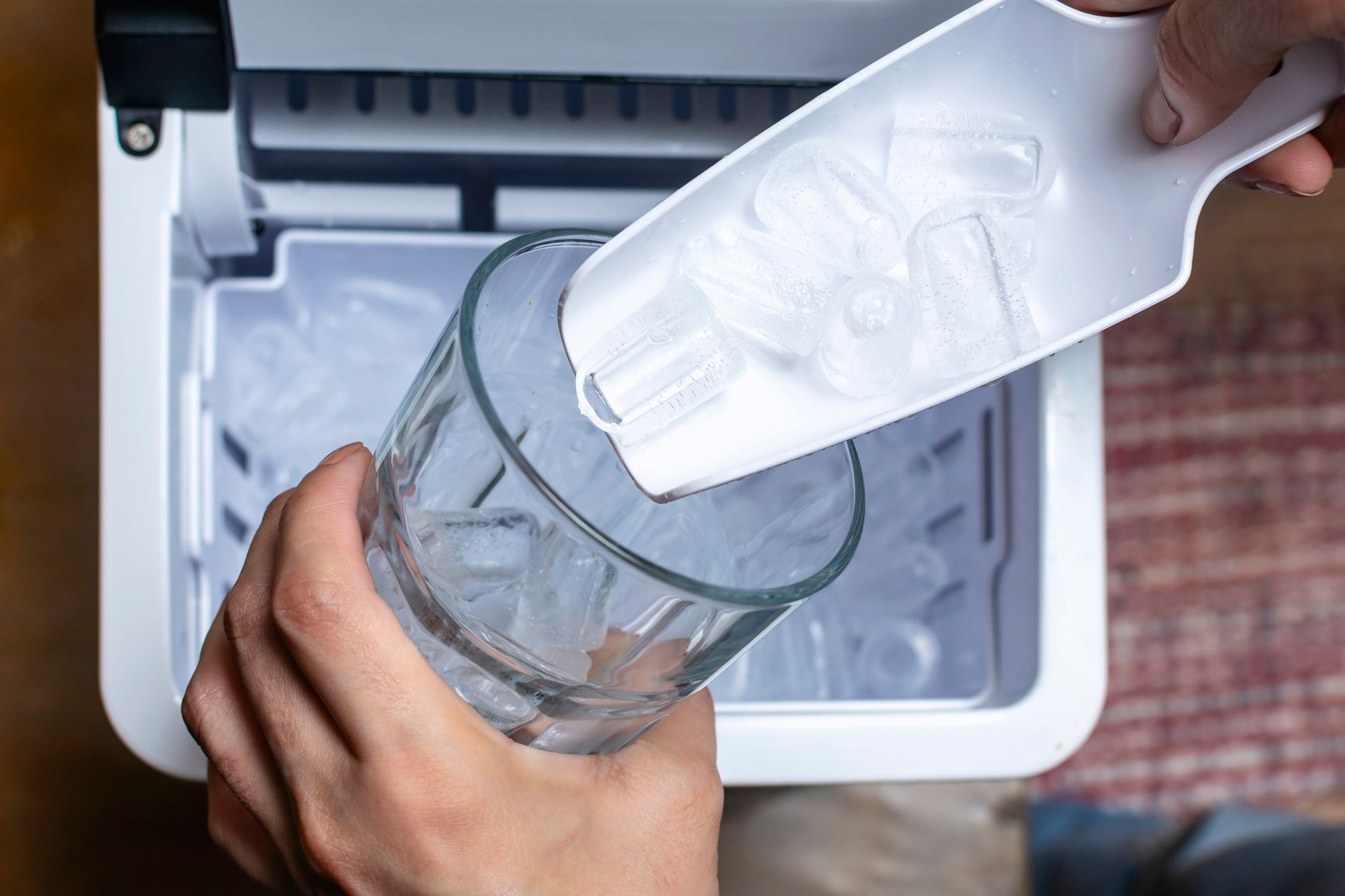A person is pouring ice into a glass from an ice maker.